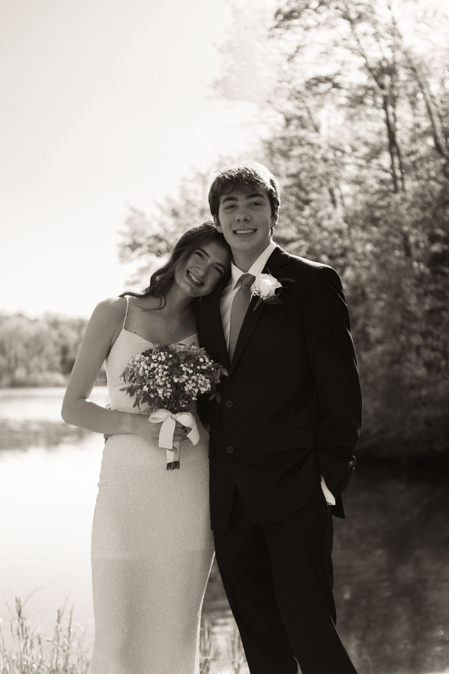 Black and white wedding photo of a couple embracing outdoors by a lake.