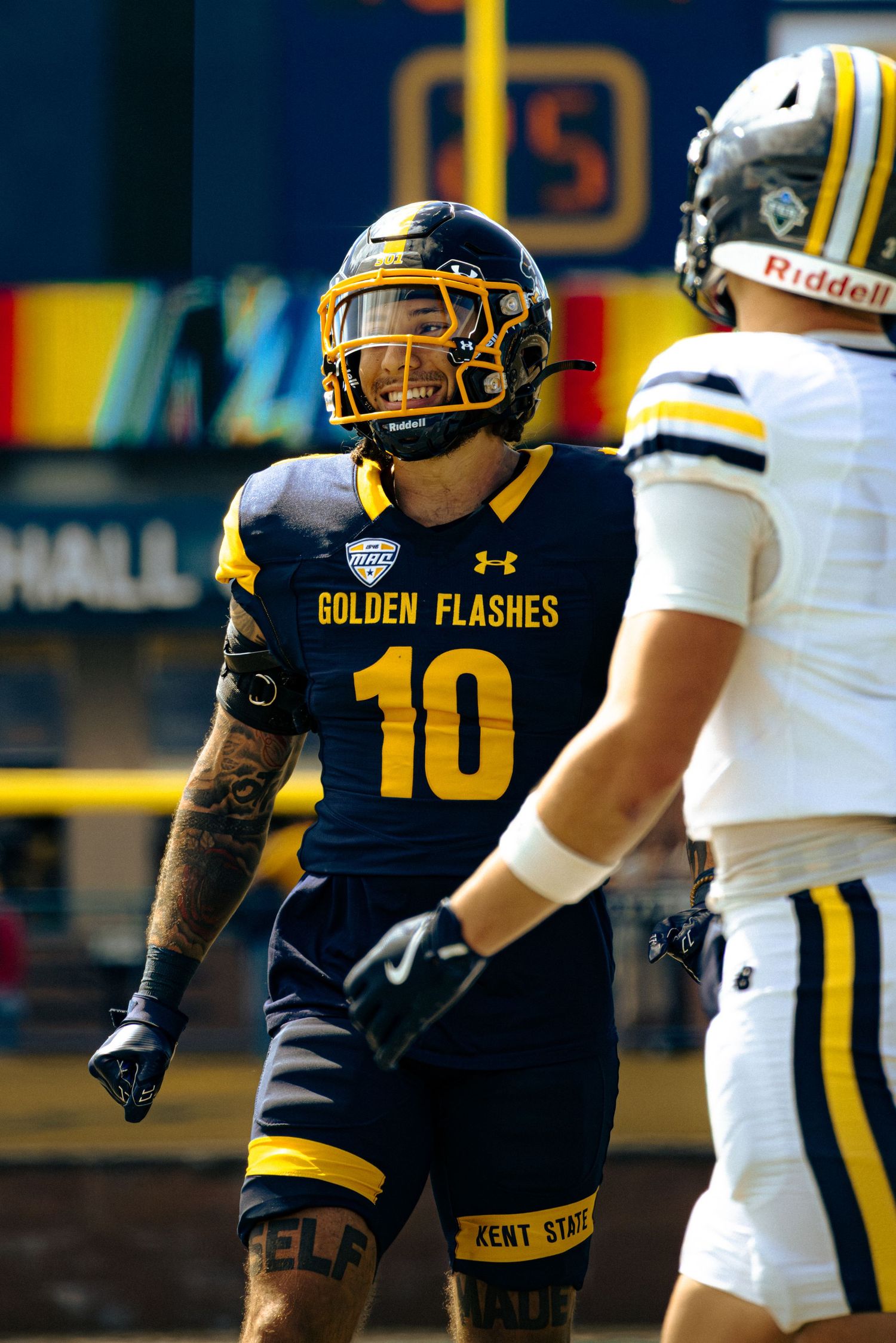Kent State football player in navy and gold uniform crouches in defensive stance during game.