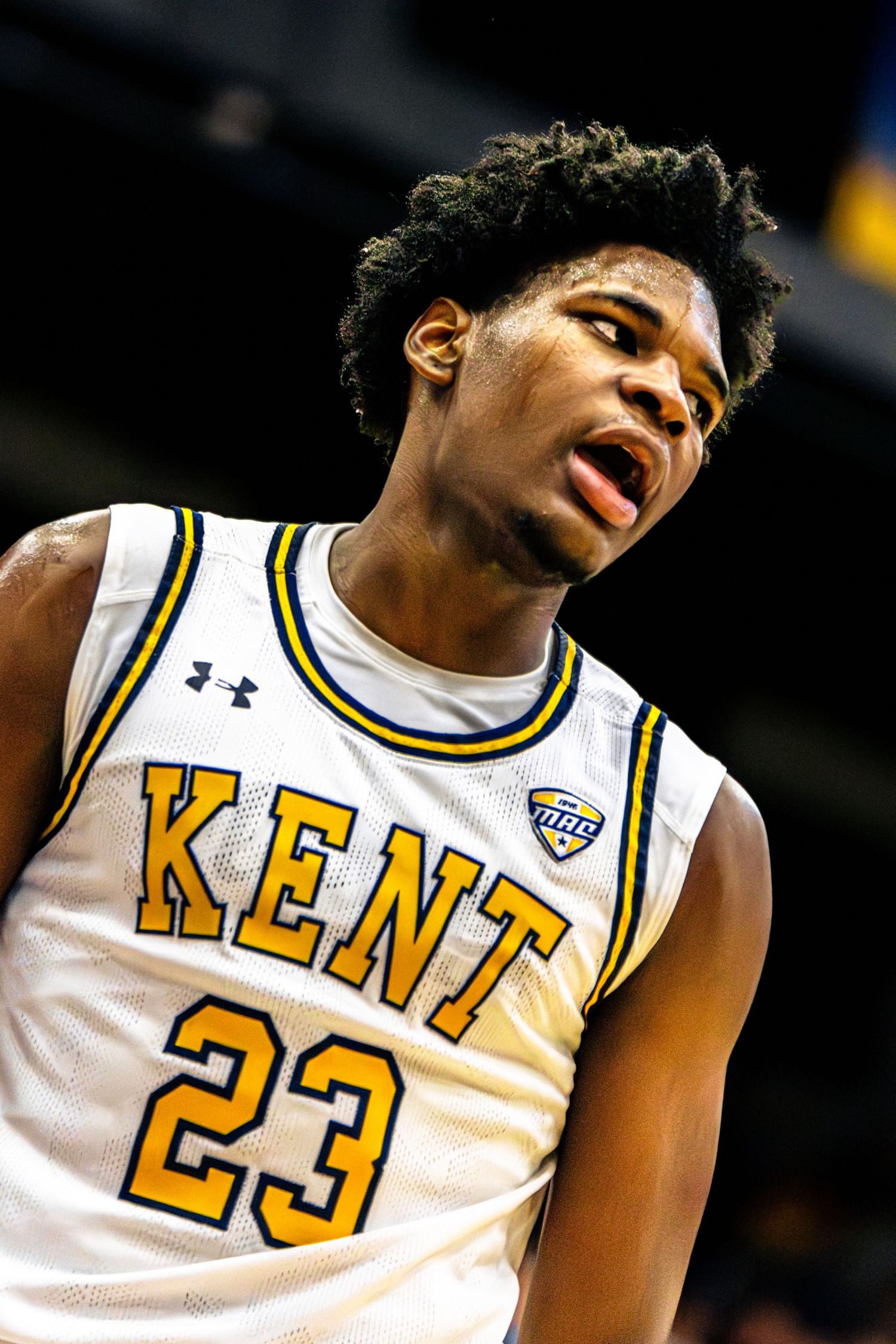 Basketball player in white and yellow Kent jersey reacts emotionally during game.