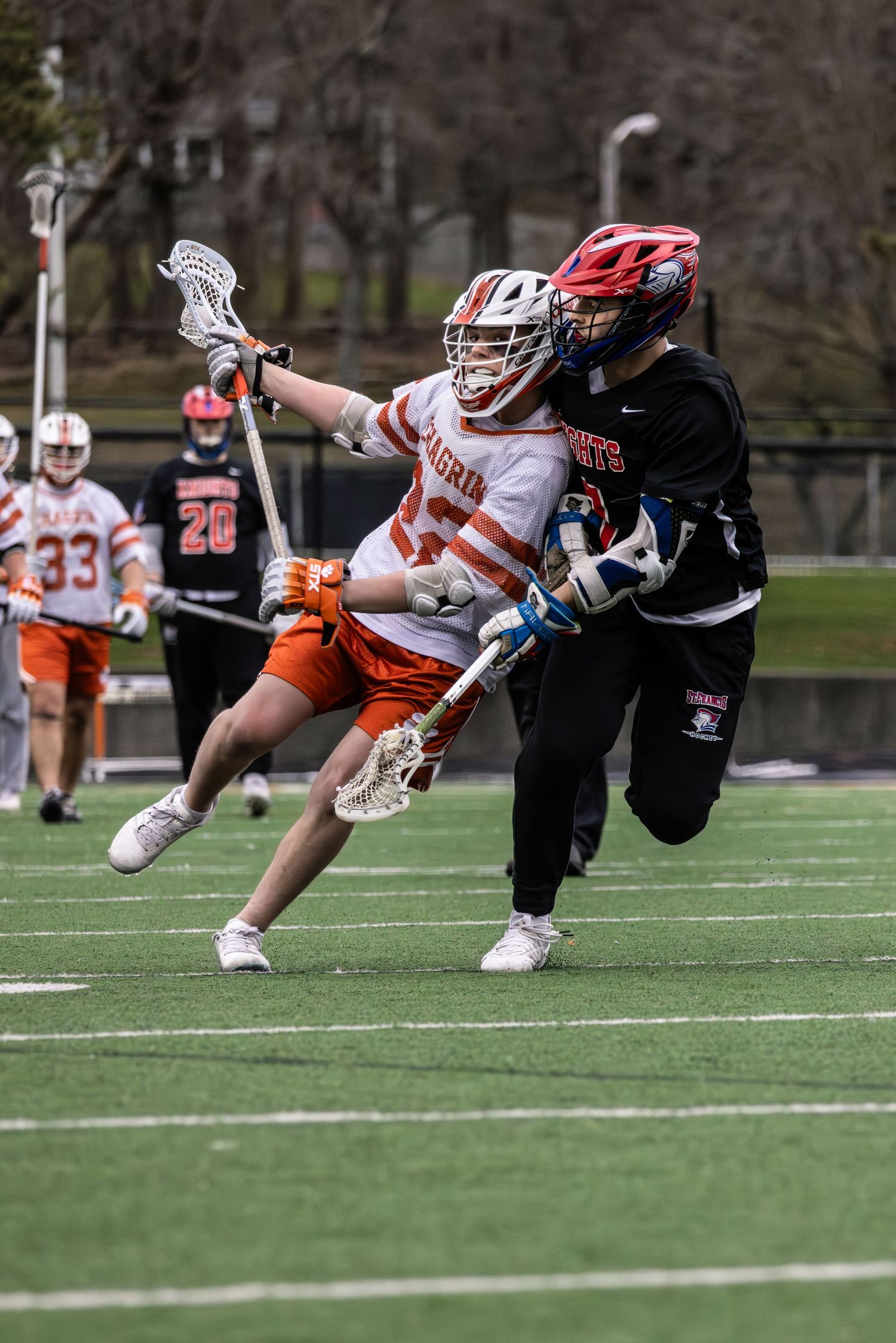Two lacrosse players in opposing colors battling for position during an intense match.