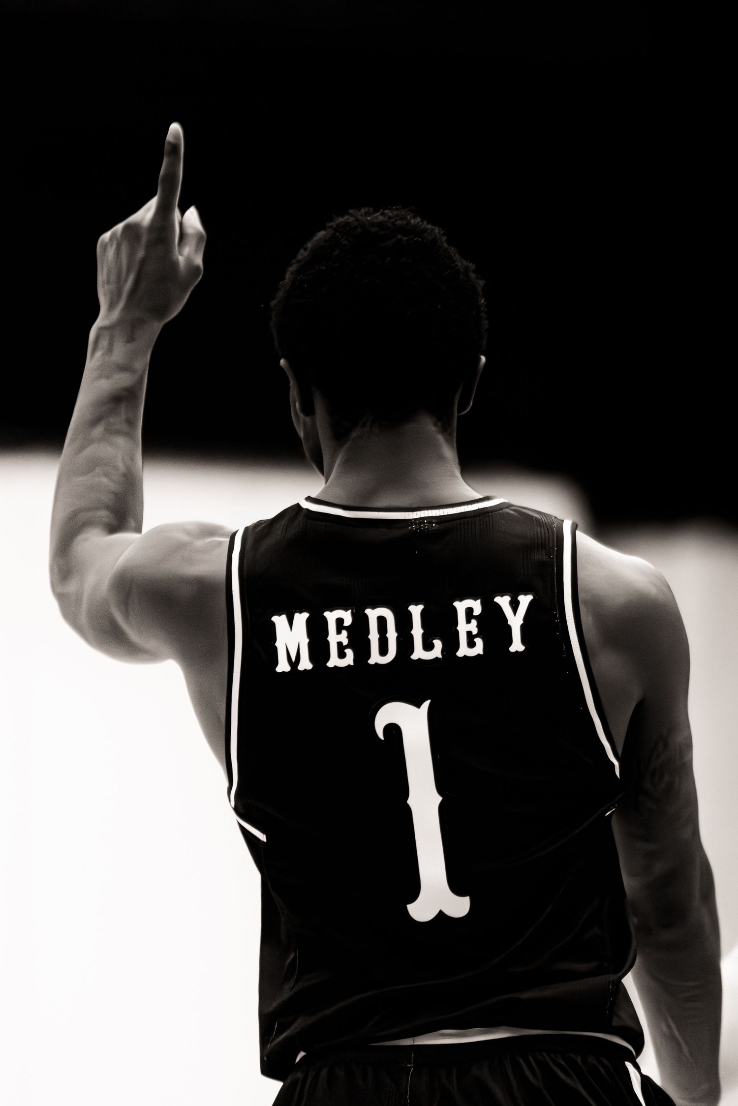 Black and white photo of basketball player wearing jersey number 1 with name Medley raising index finger skyward.