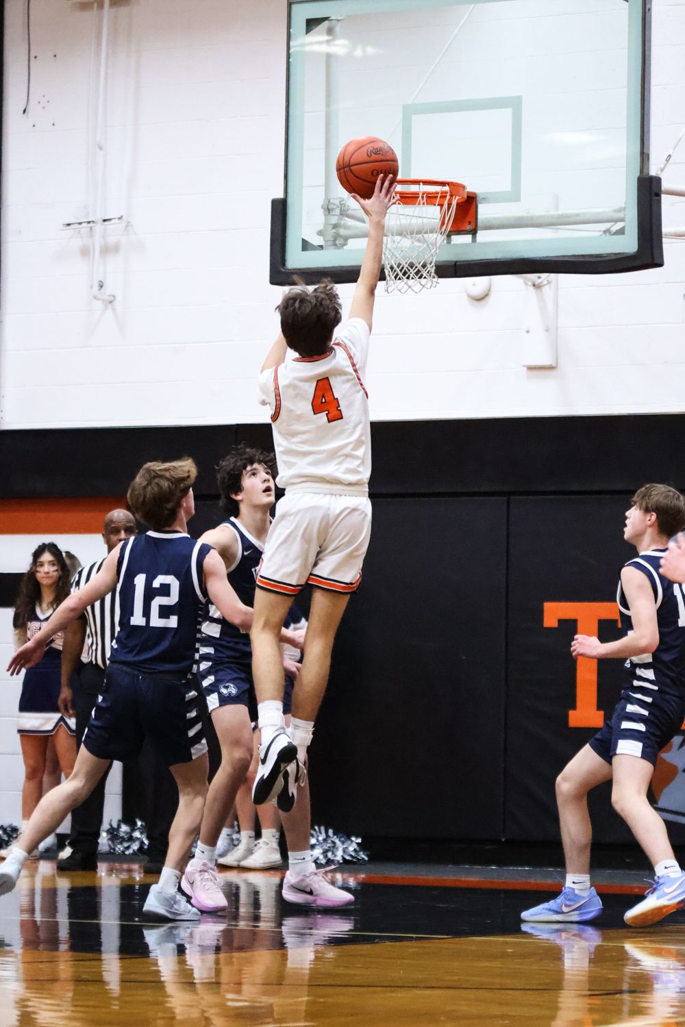 Basketball player in white jersey leaps for layup during indoor game.