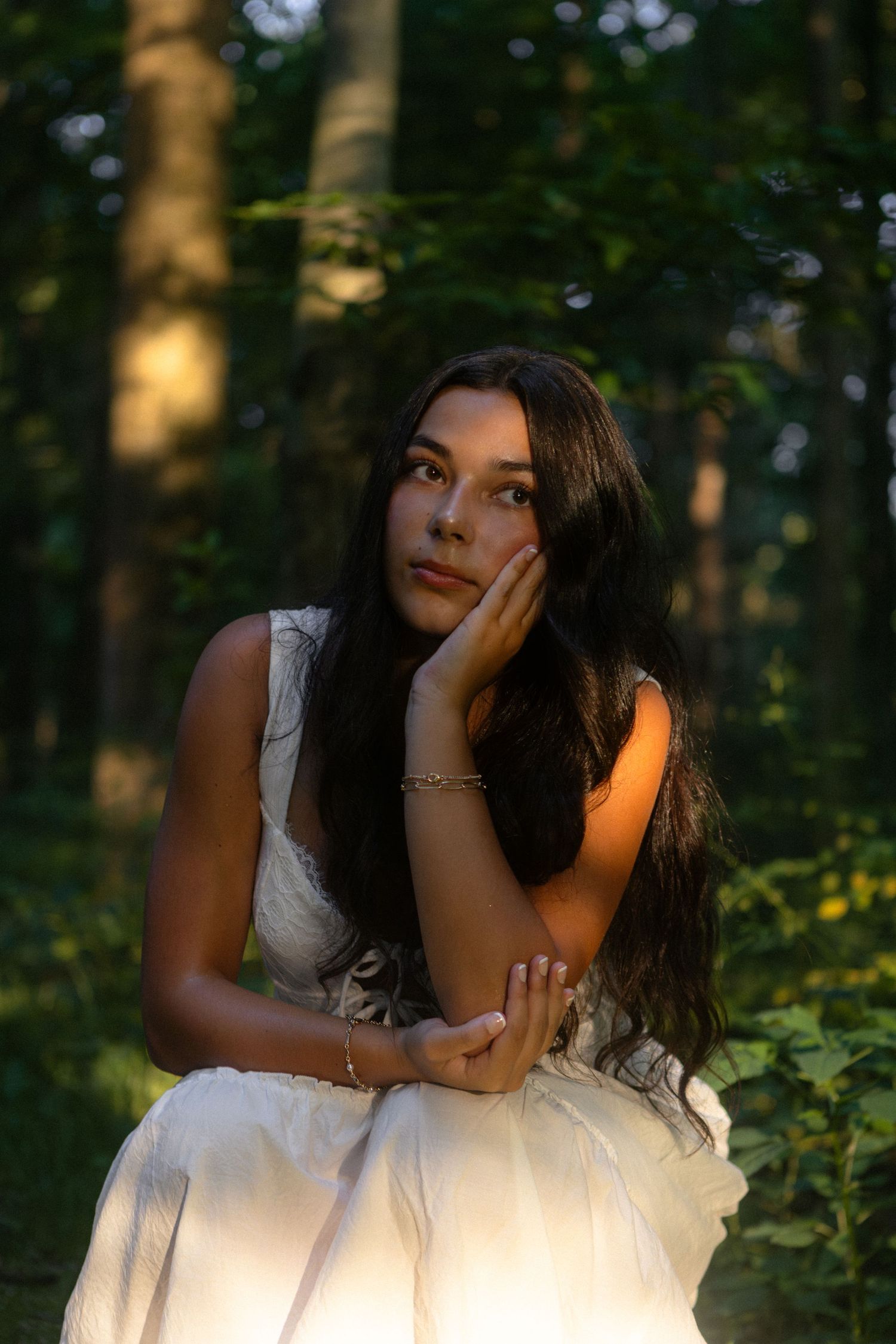 A person in a white dress poses gracefully in a sunlit forest setting, creating a dreamy artistic portrait series.