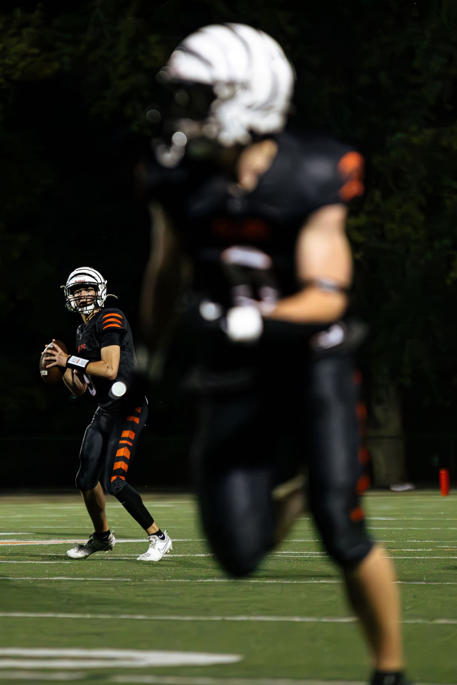 Football players in black and orange uniforms practicing drills on a sunny field during training camp.