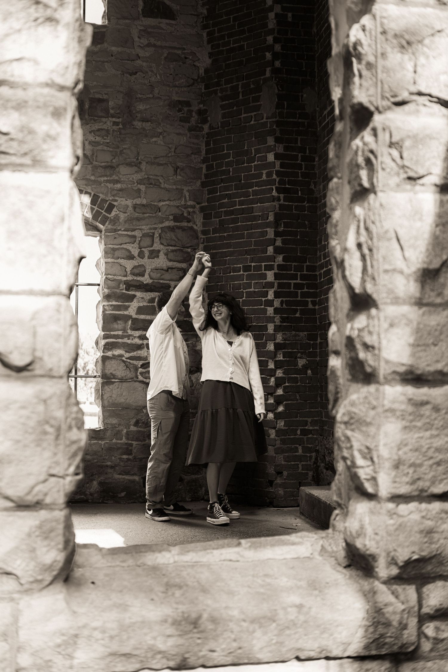 Two people sit in a stone archway of an old brick building creating a dramatic black and white composition.