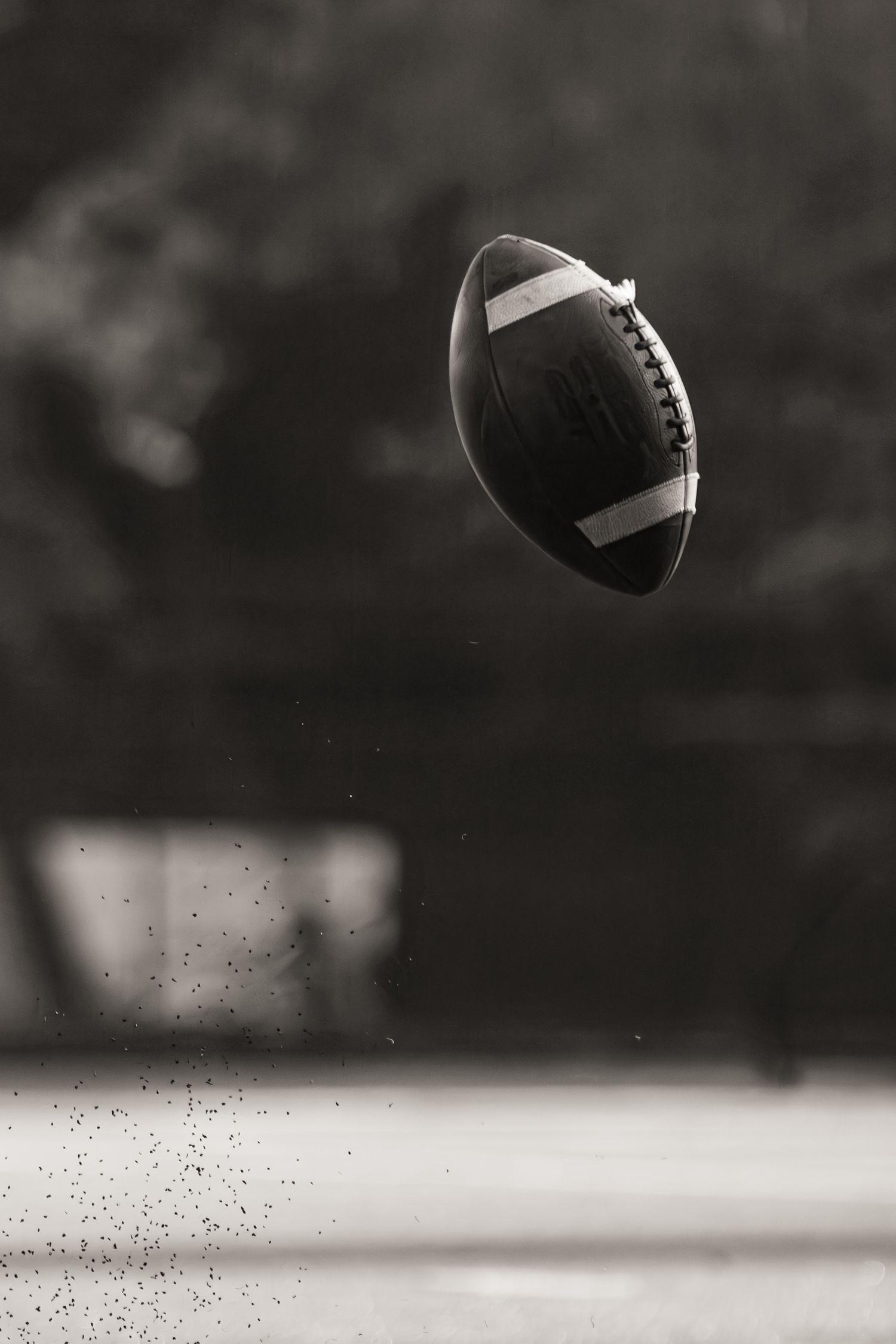 Black and white photo of a football flying through the air during a game.