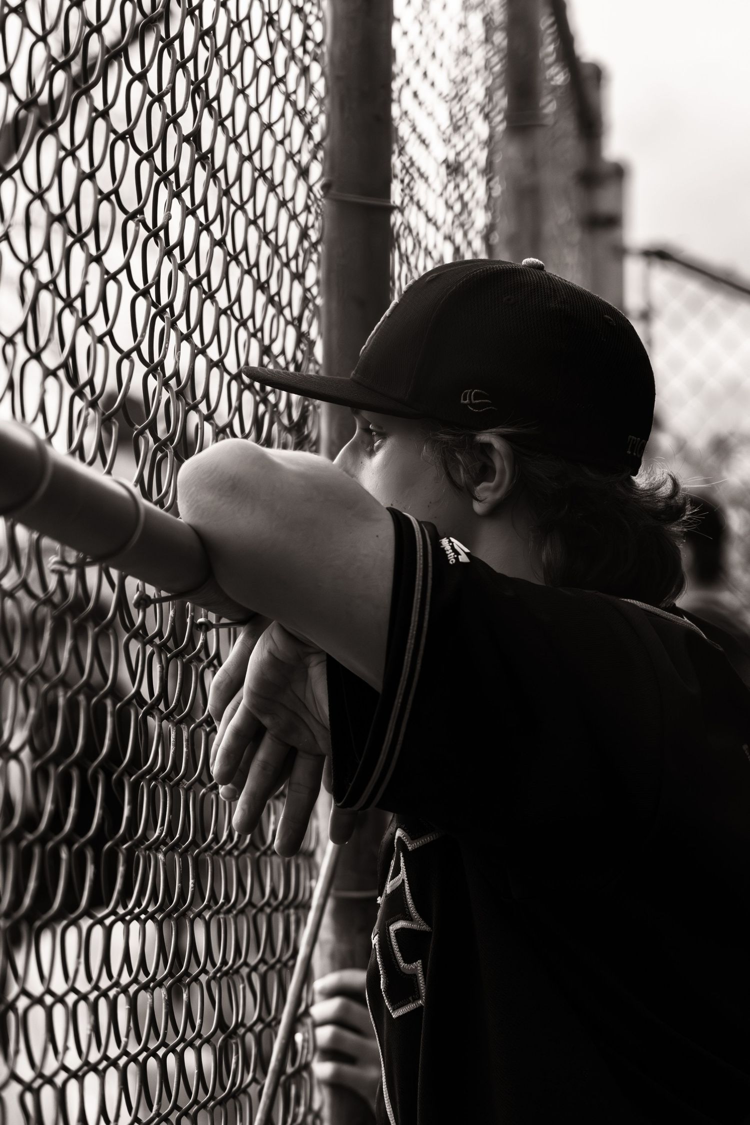 Silhouetted baseball players stare through chain link fence in black and white.
