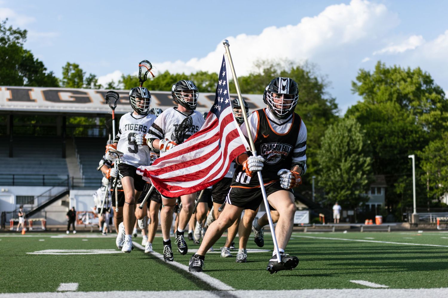 Cheerleaders performing with American flags on a sports field during a sunny day.