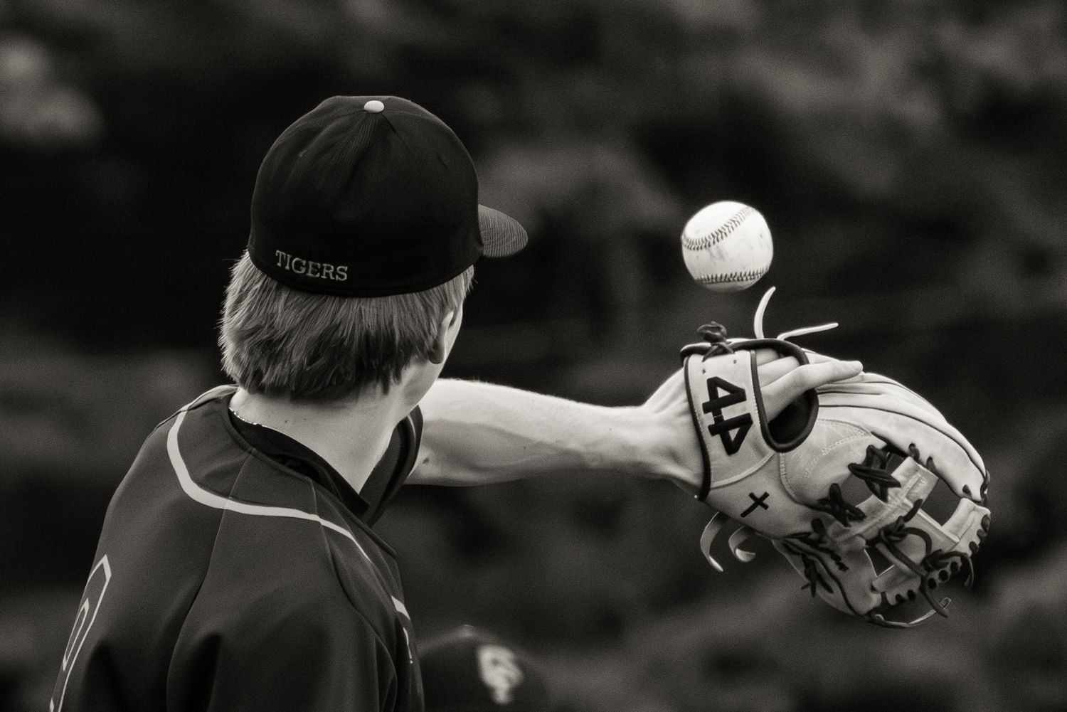 Baseball player in black uniform catching ball in glove, shown in black and white.