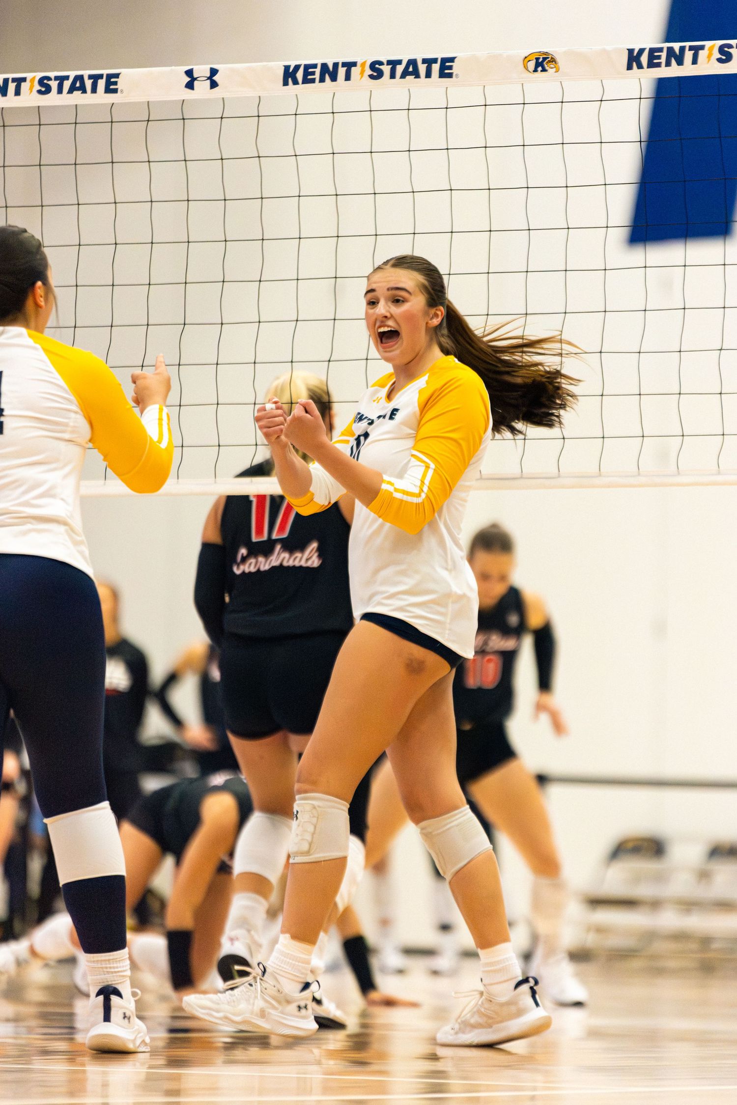 Volleyball players in yellow and white uniforms jump and celebrate during an intense match at Kent State.