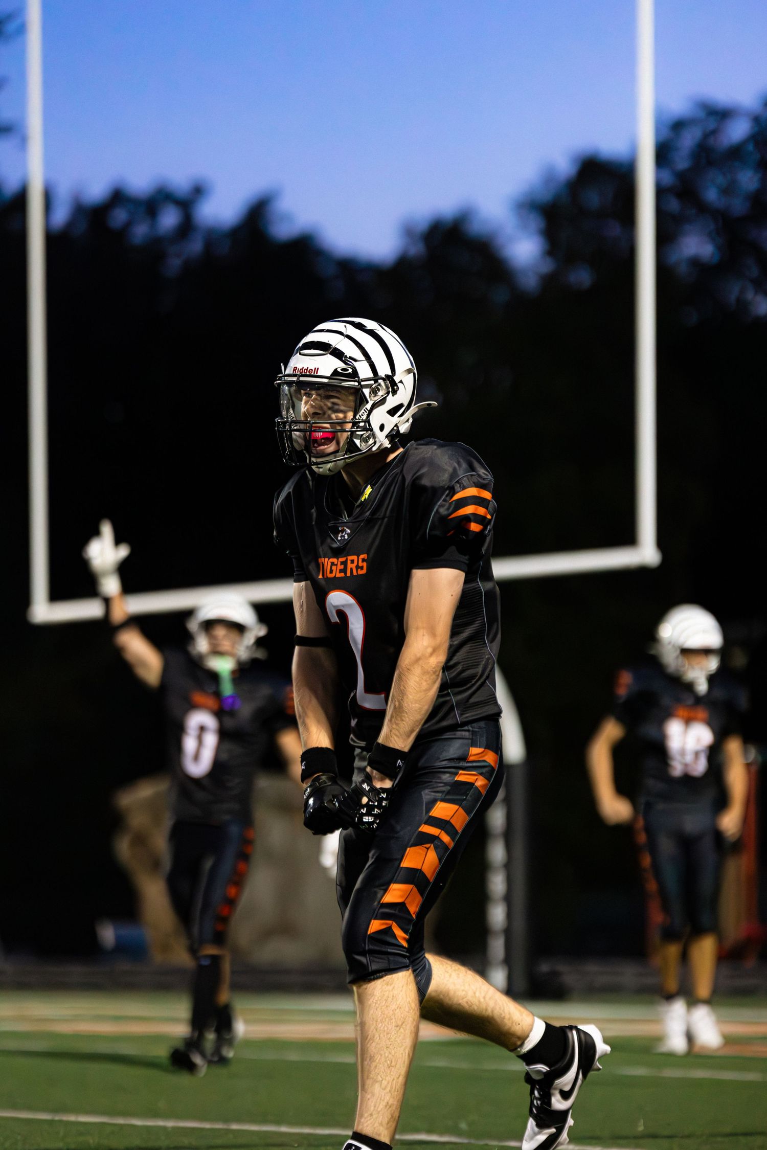 Football player runs on field wearing black uniform and knee brace during evening practice session.