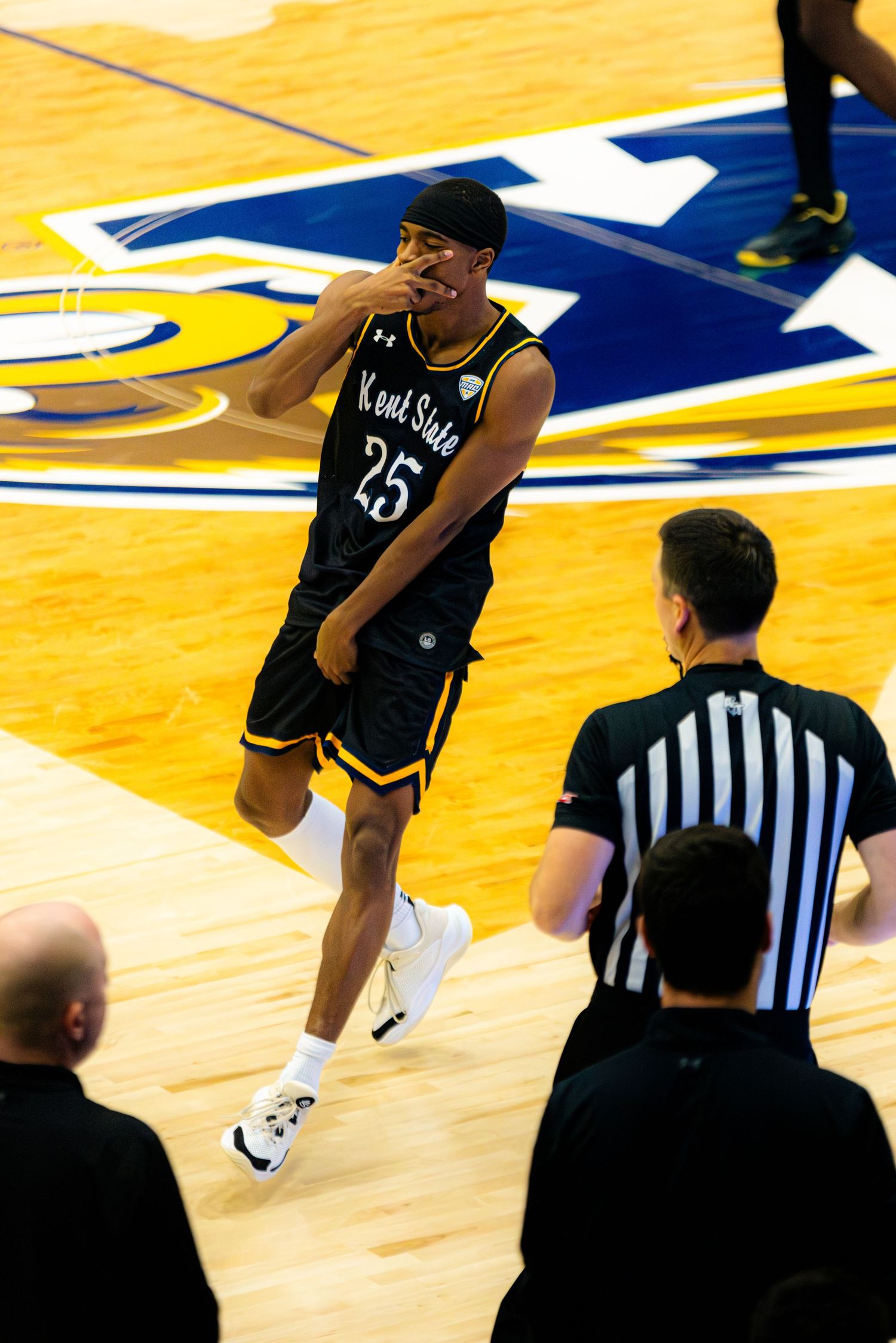 Basketball player in black jersey number 23 dribbling on yellow court with referee in striped uniform watching.