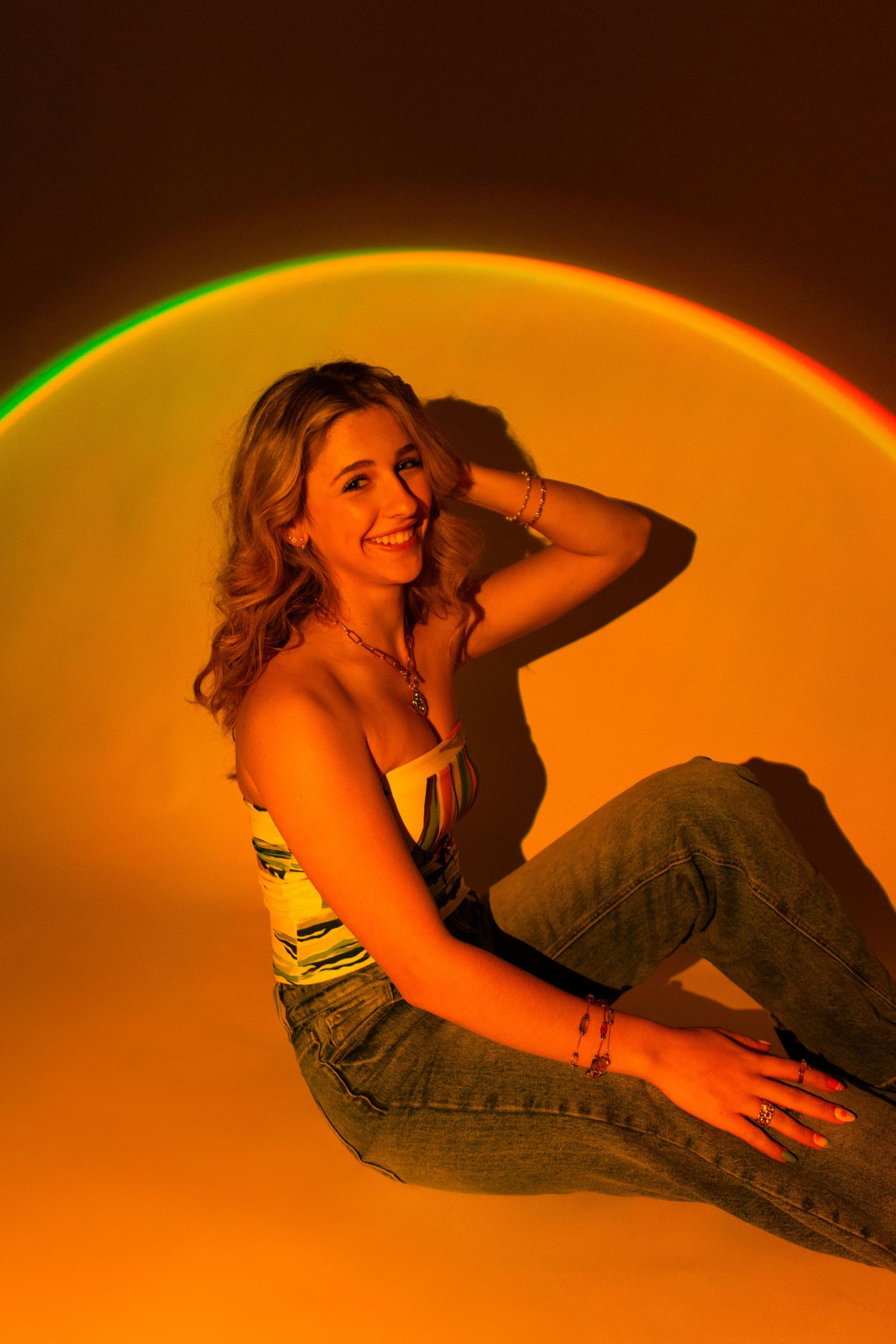 A woman in denim jeans reclines in an artistic orange-lit silhouette pose against a dark background.