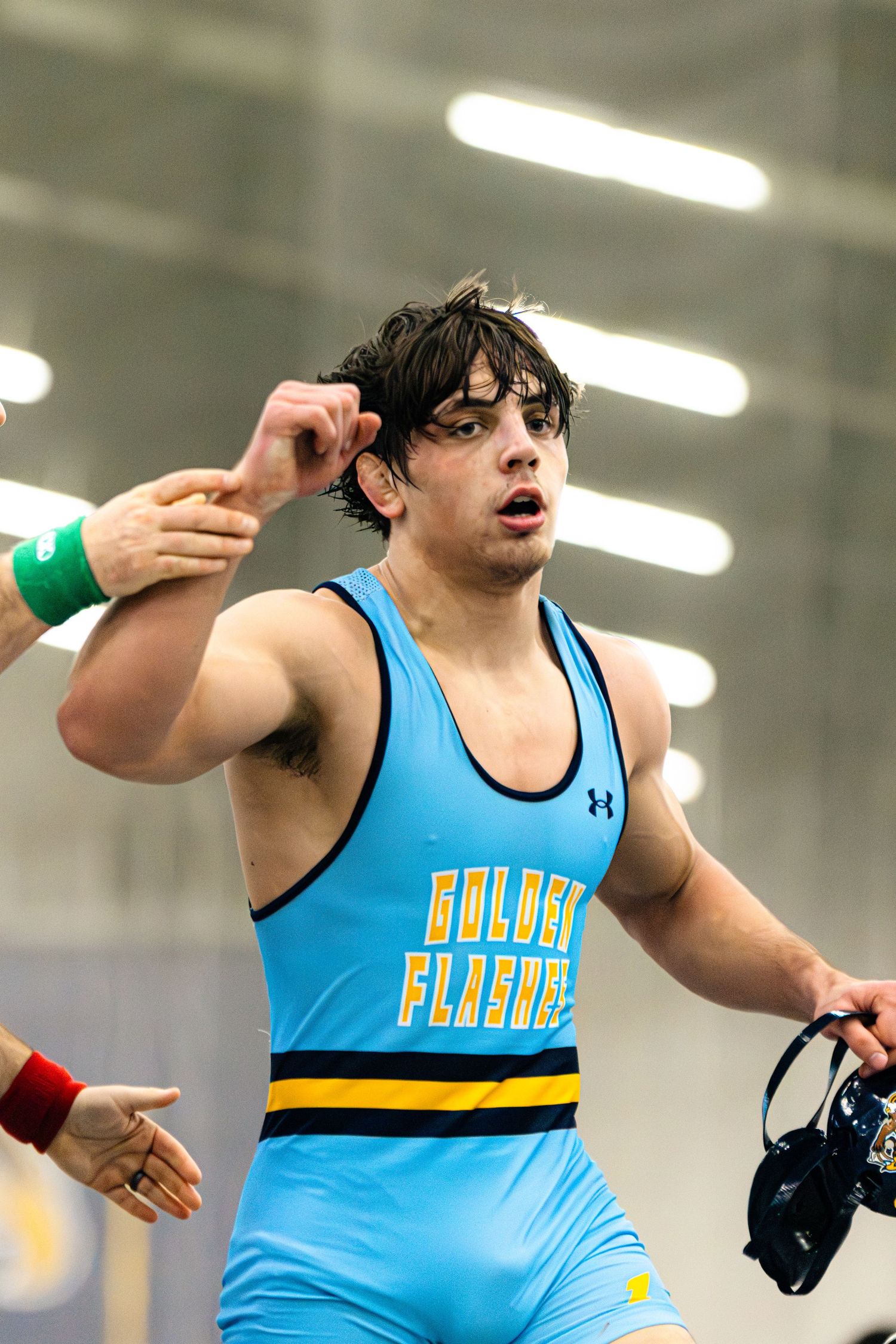 High school wrestler in light blue uniform performs dynamic movement during competitive match.