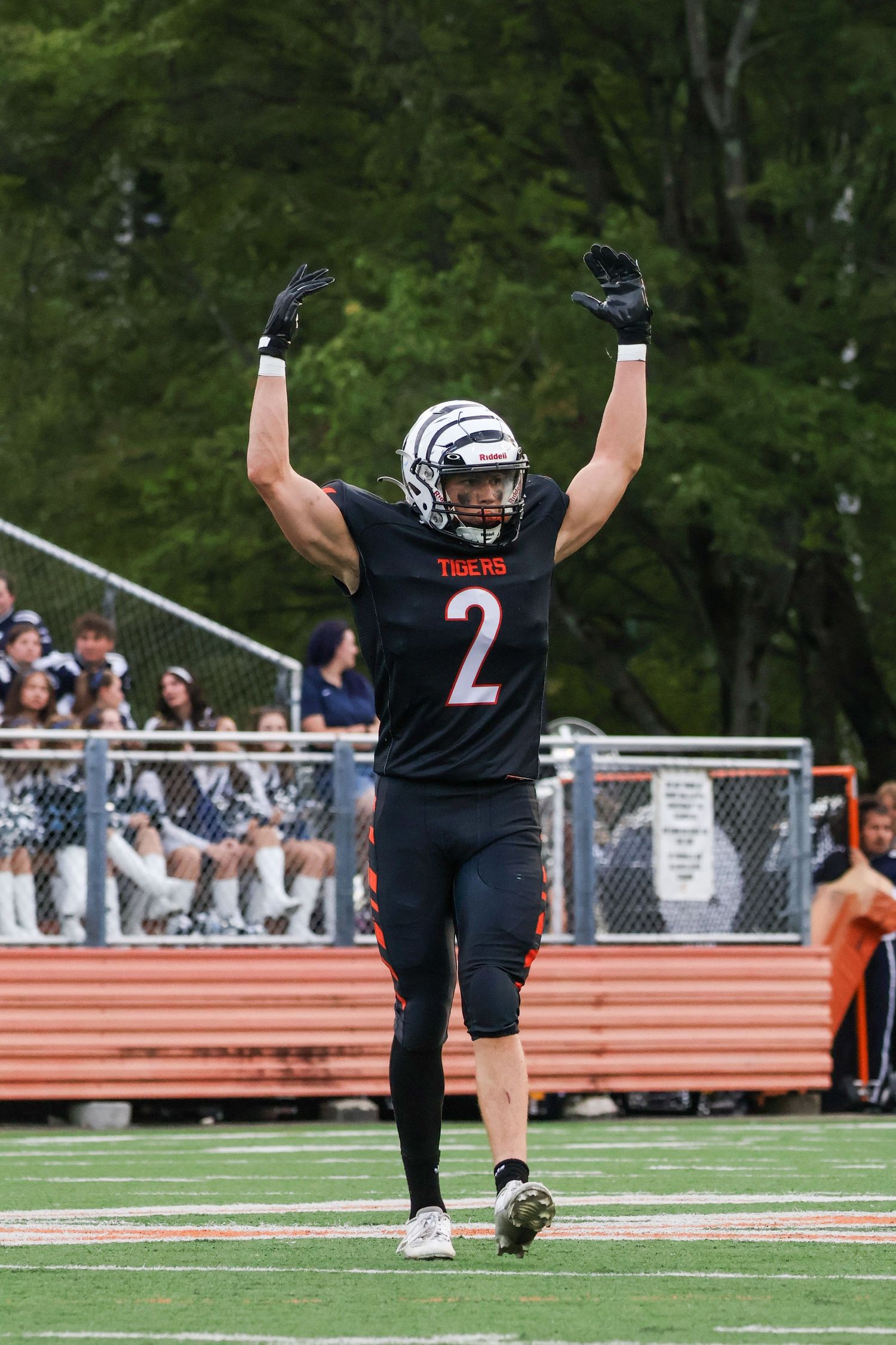 Football player in black uniform number 2 celebrates with raised arms on field.