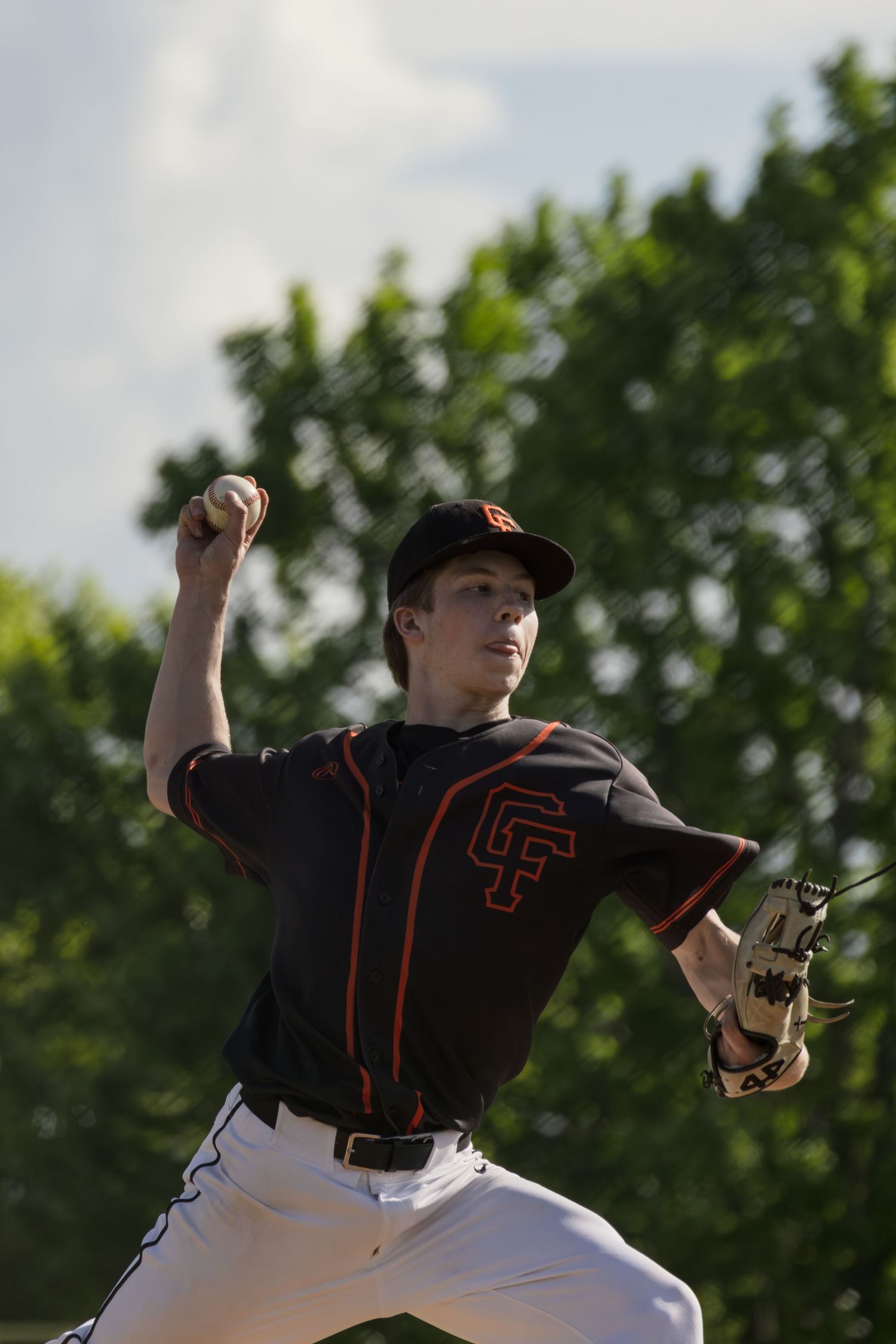 Baseball player in black and orange uniform winds up to throw a pitch during a game.