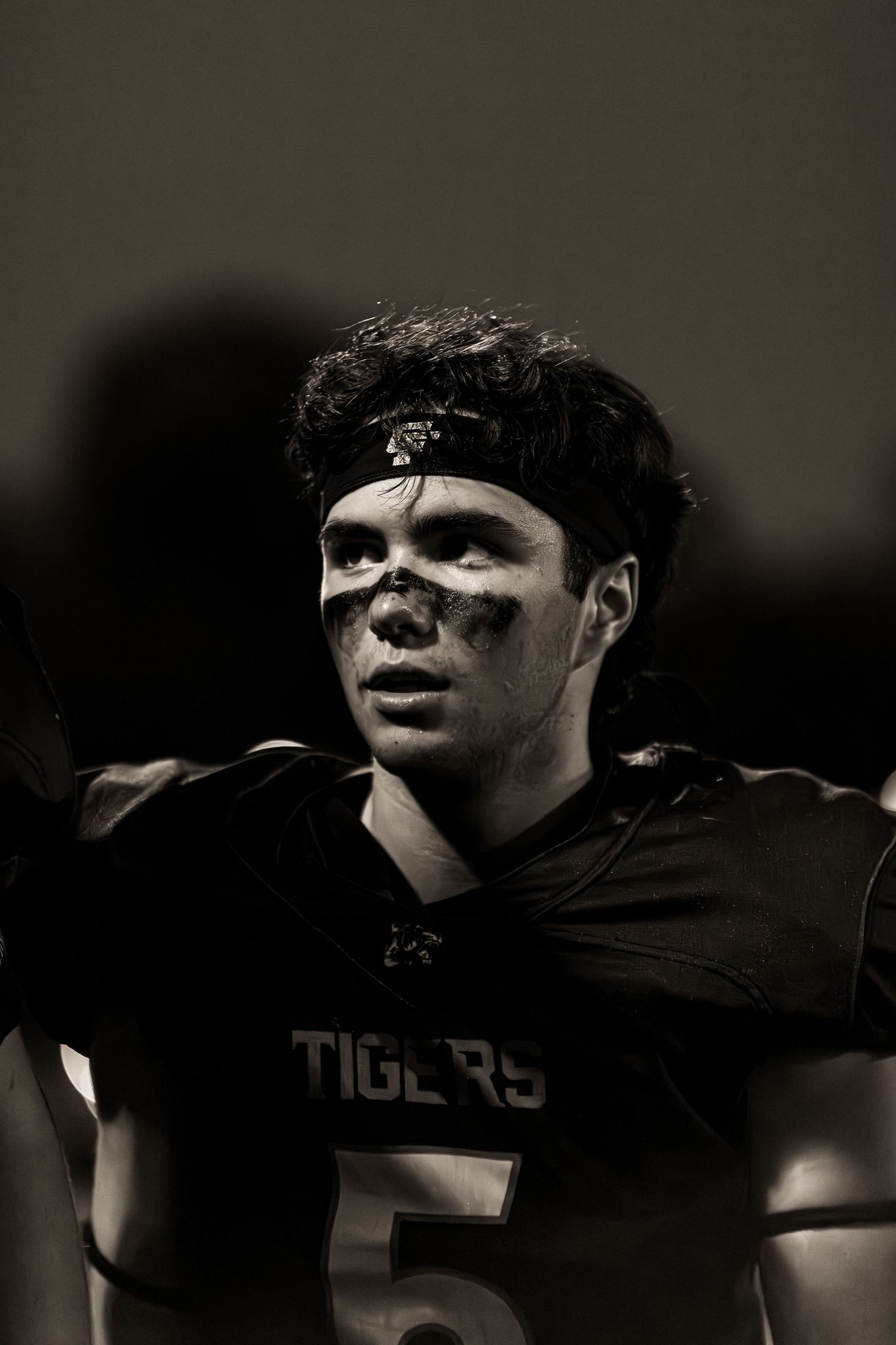 Black and white photo of a football player wearing a Tigers jersey in dramatic lighting during a game.