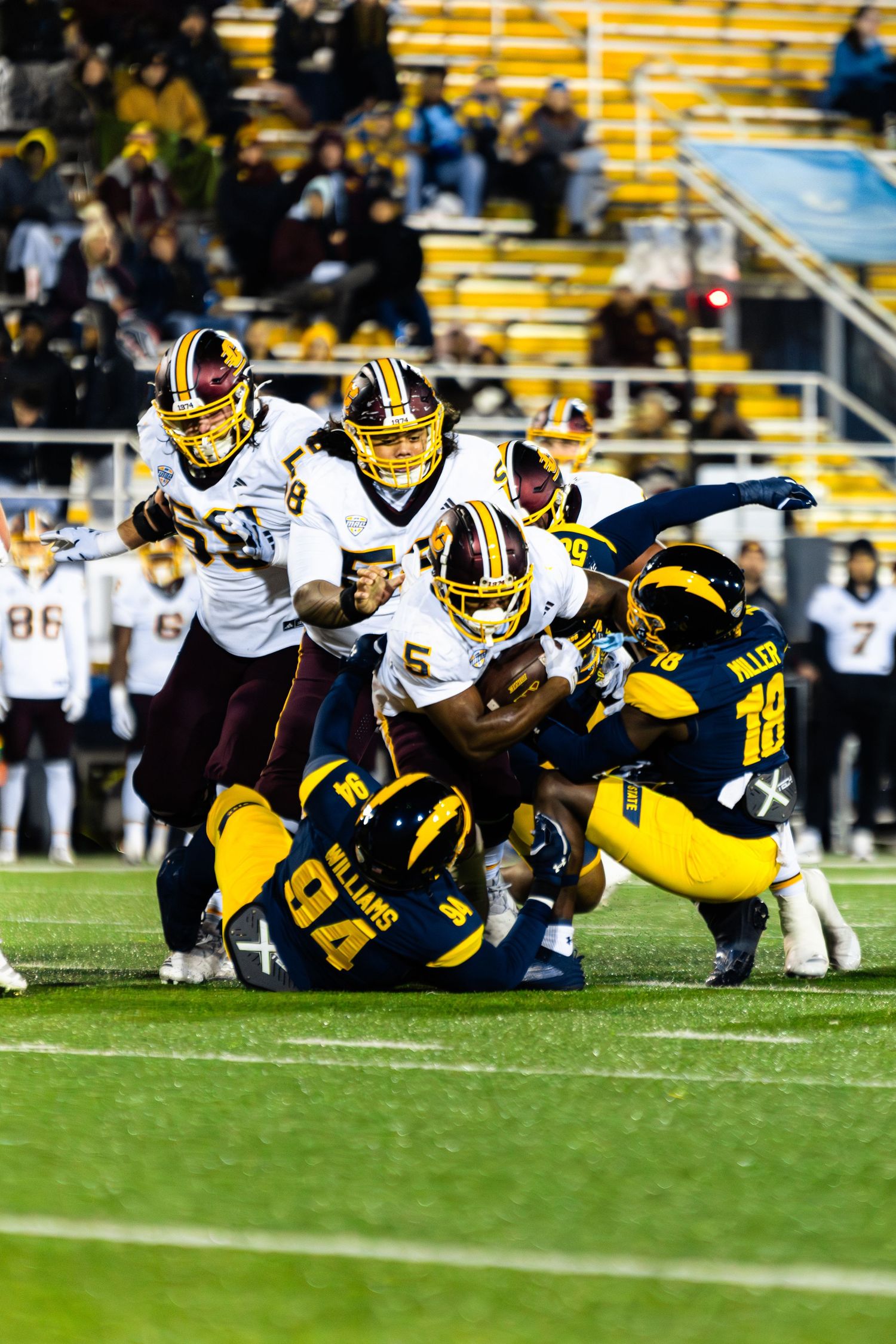 Football players in yellow and white uniforms dive and tackle during an intense play on the field.