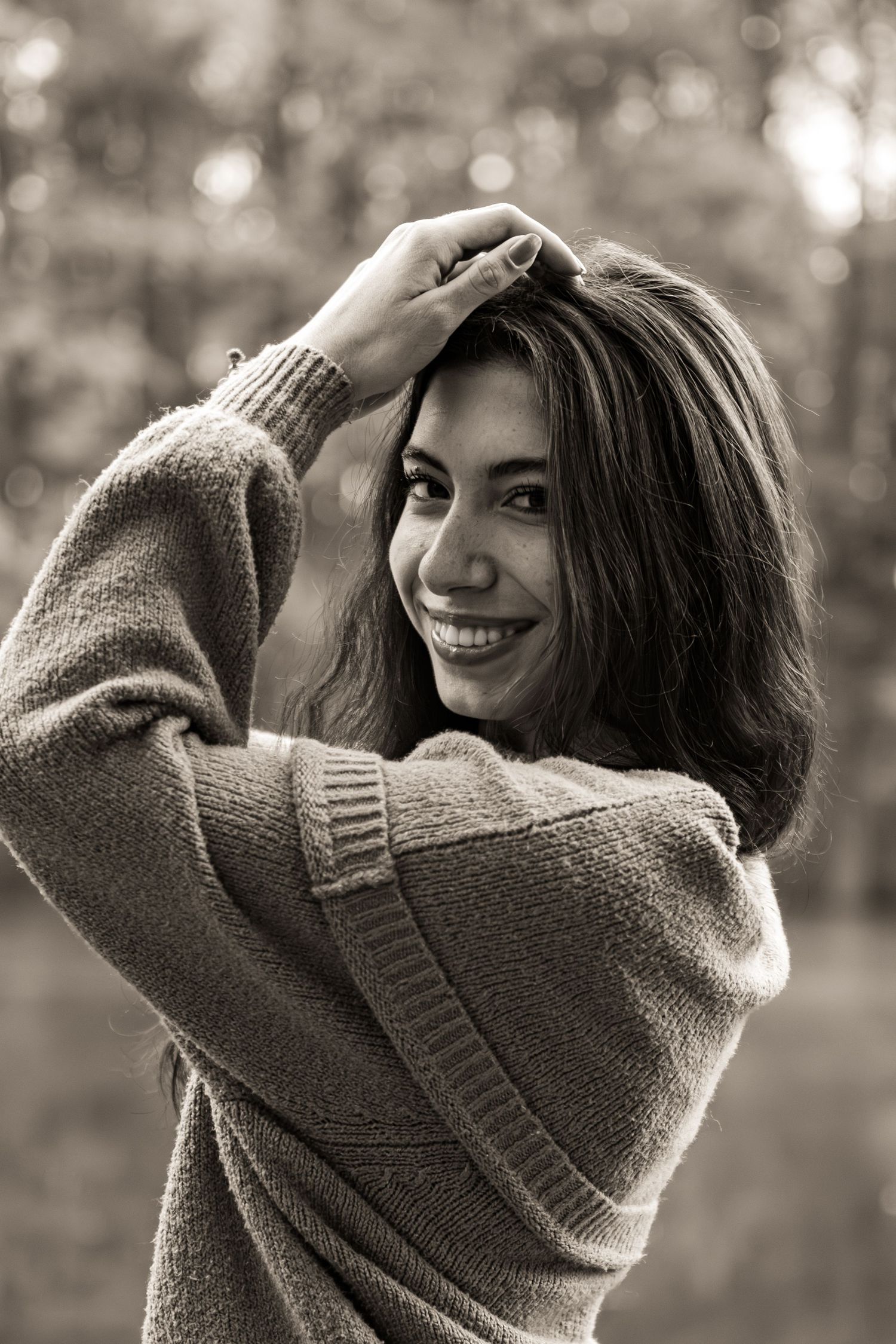 A person in a cozy sweater smiles while posing outdoors in a series of black and white photos.
