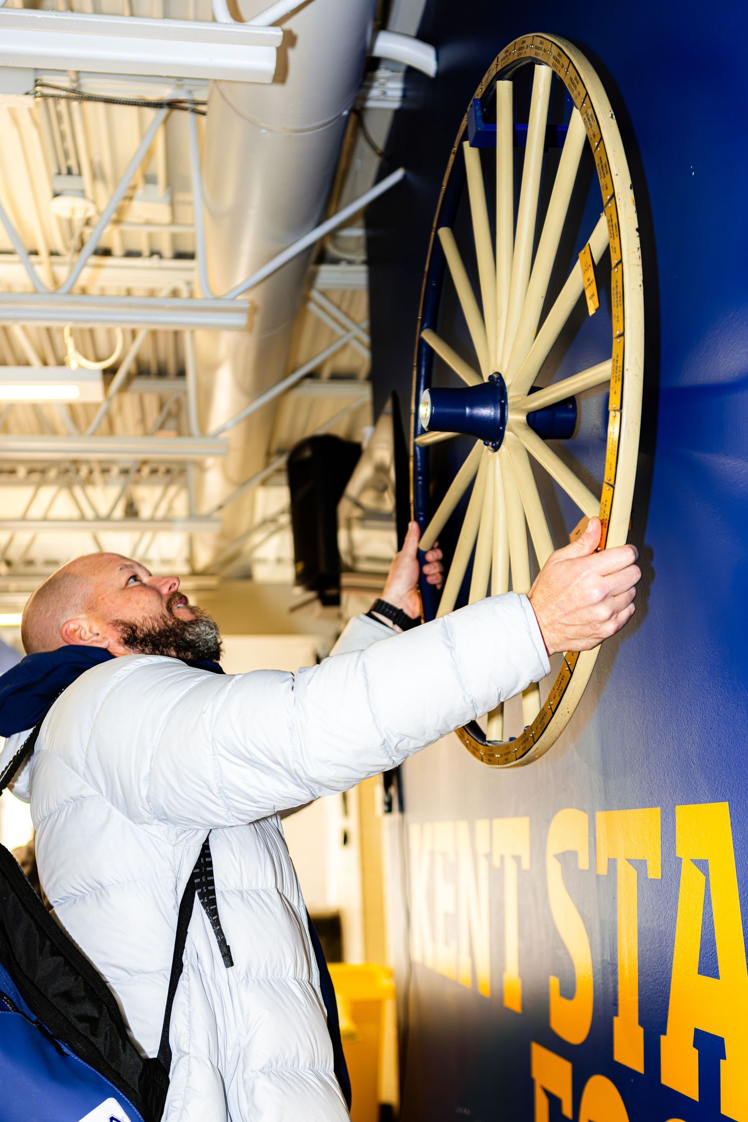 A person in a white shirt spins a large golden wagon wheel mounted on a wall with blue and yellow decor.