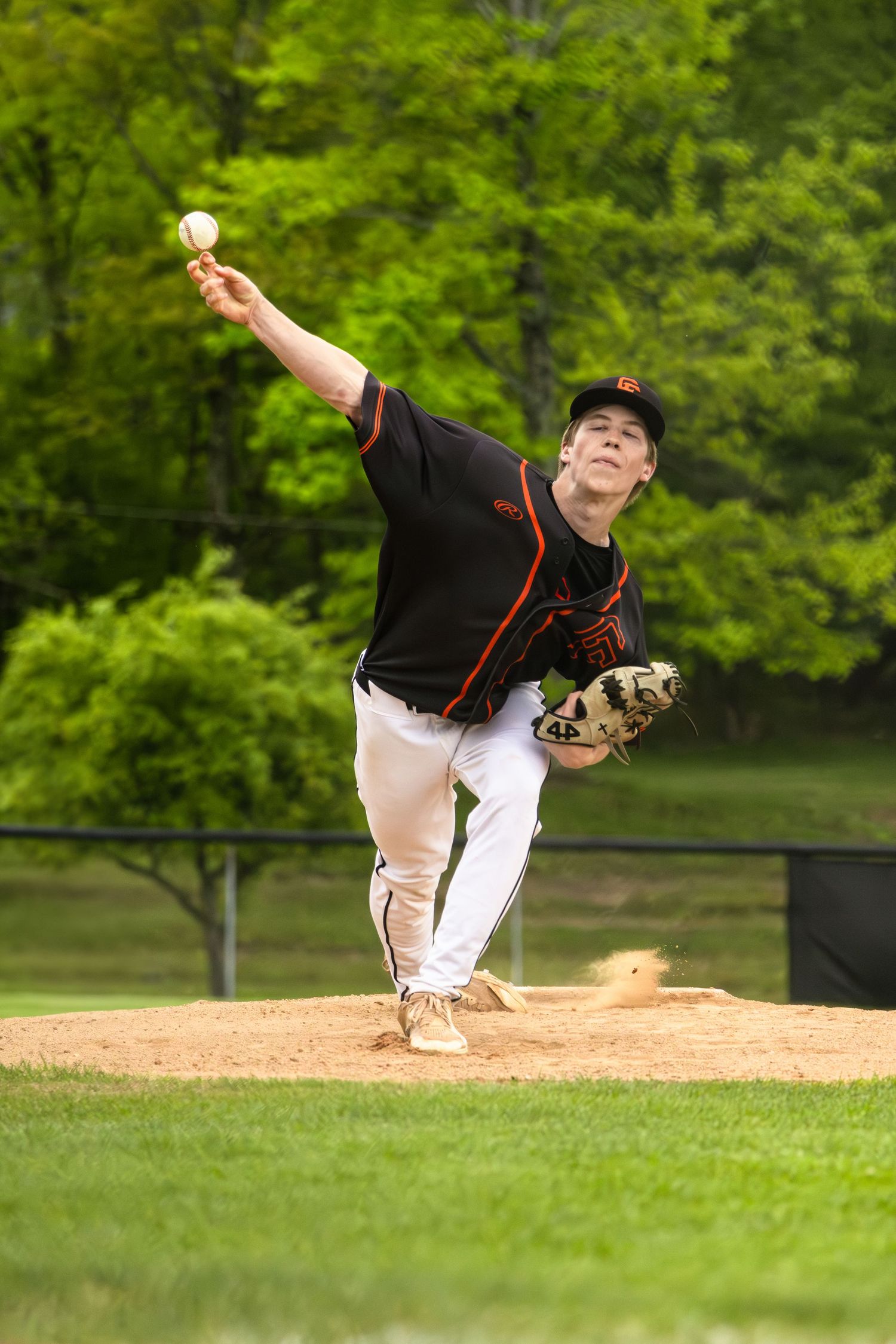 Baseball player in black uniform demonstrating pitching motion sequence on green field.