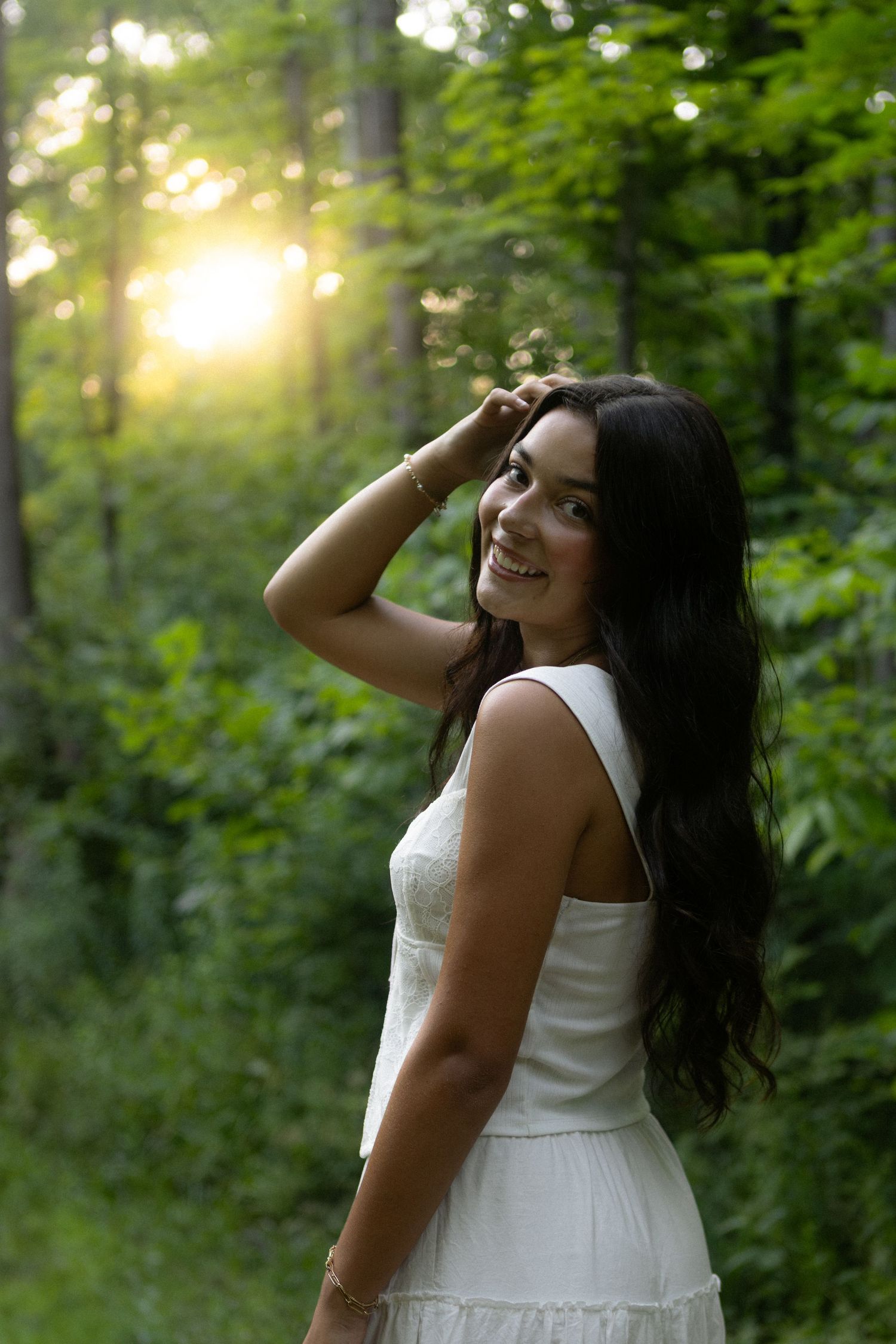 A white summer dress glows in dreamy golden sunlight filtering through lush green forest foliage.