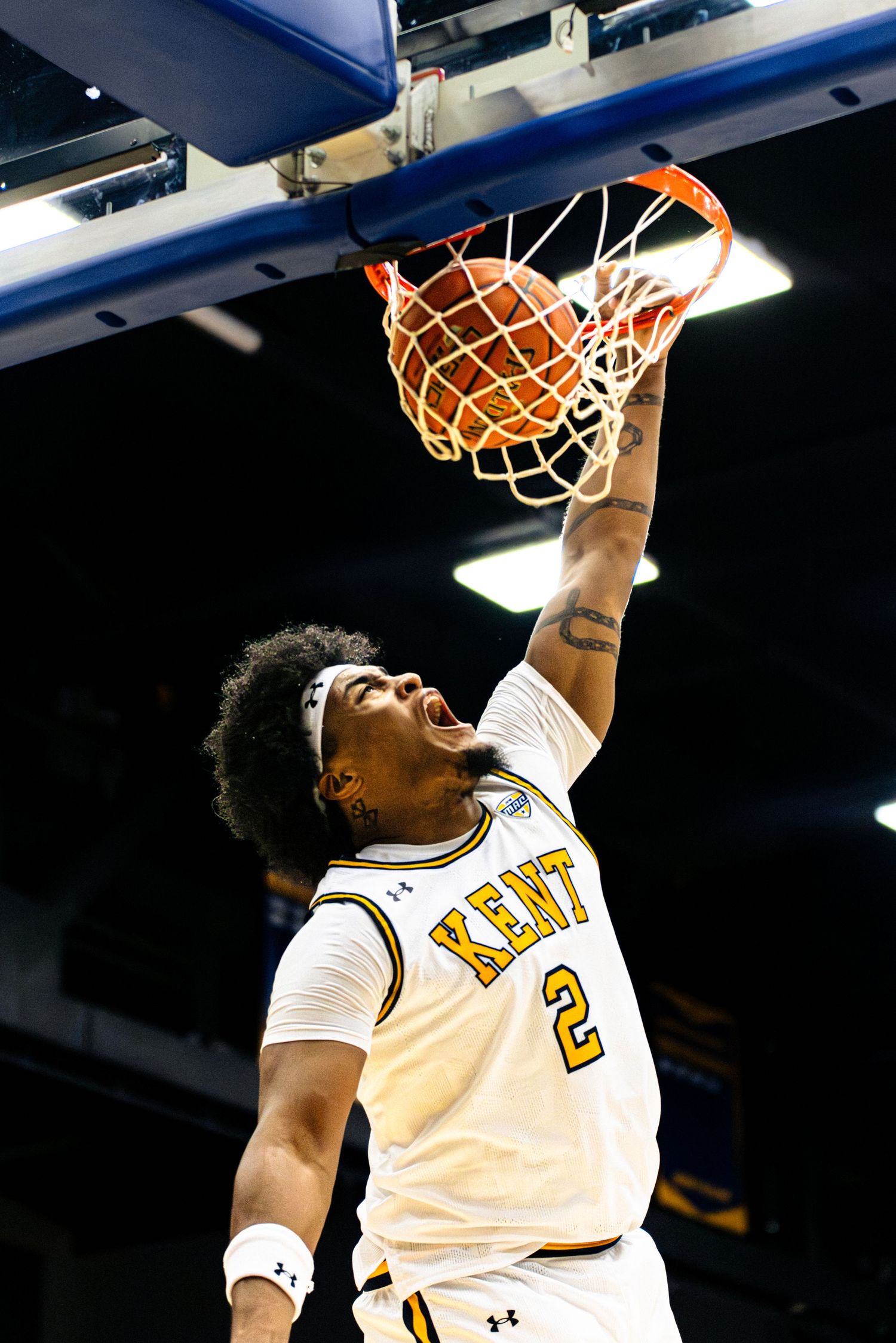 Basketball player in white Kent State jersey dunks the ball during an intense game moment.