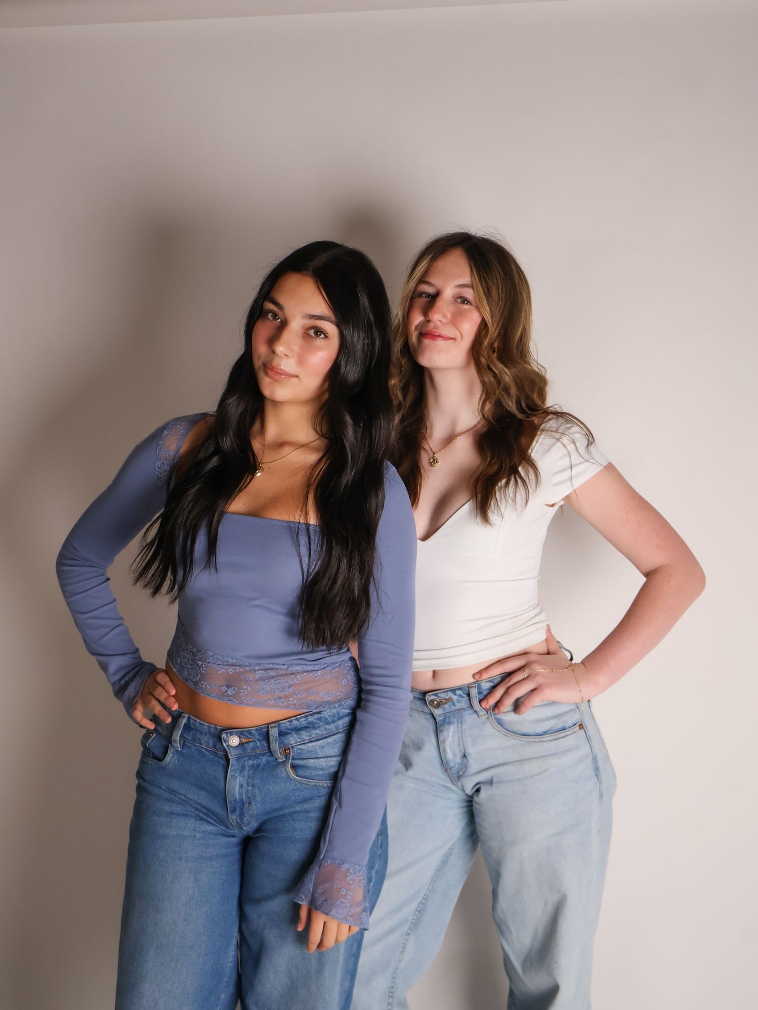 Two friends wearing denim jeans and casual tops pose together against a light-colored wall in a series of photos.