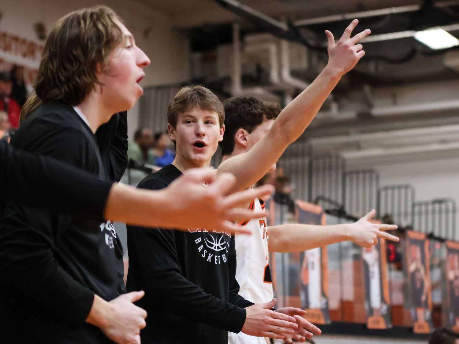 Athletes celebrating and cheering on sidelines during indoor sports event.