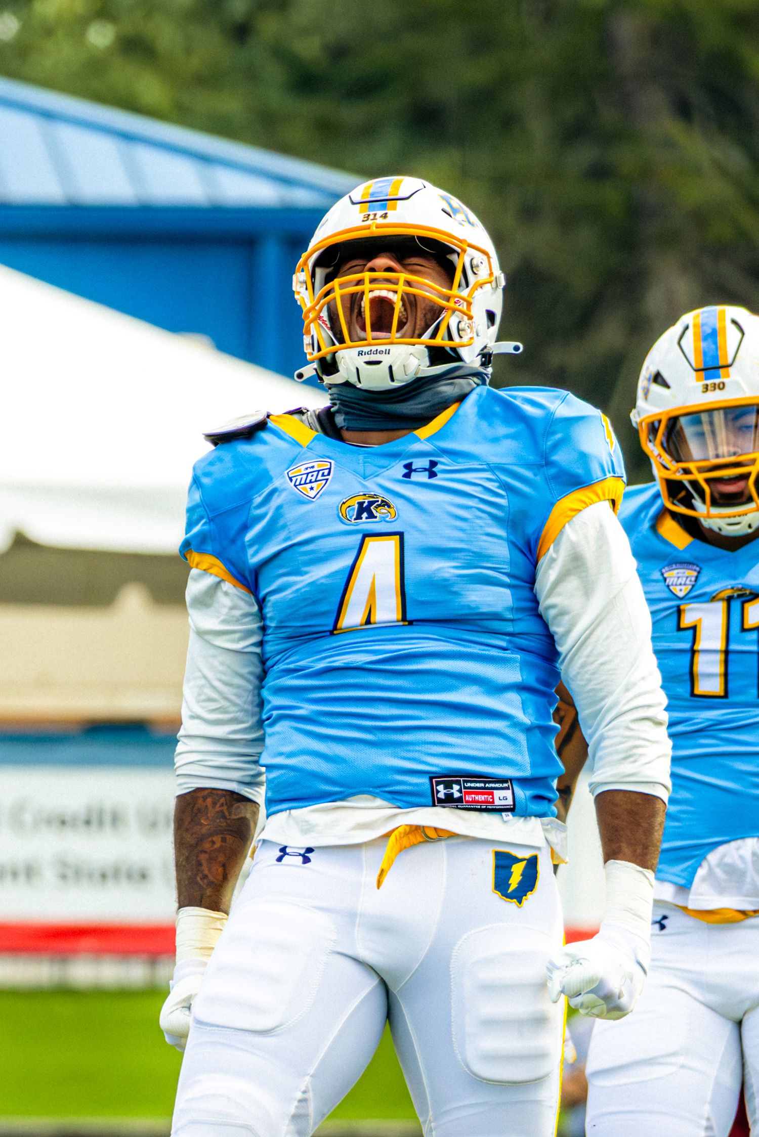 Football players wearing blue and white uniforms with gold helmets walk together on a sports field.