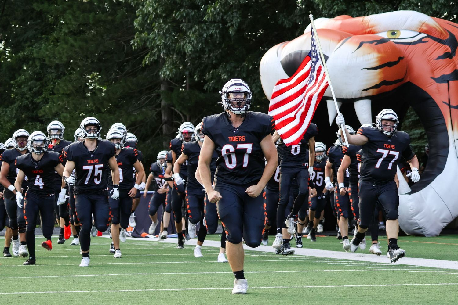High school football team entrance with player carrying American flag through inflatable tunnel.