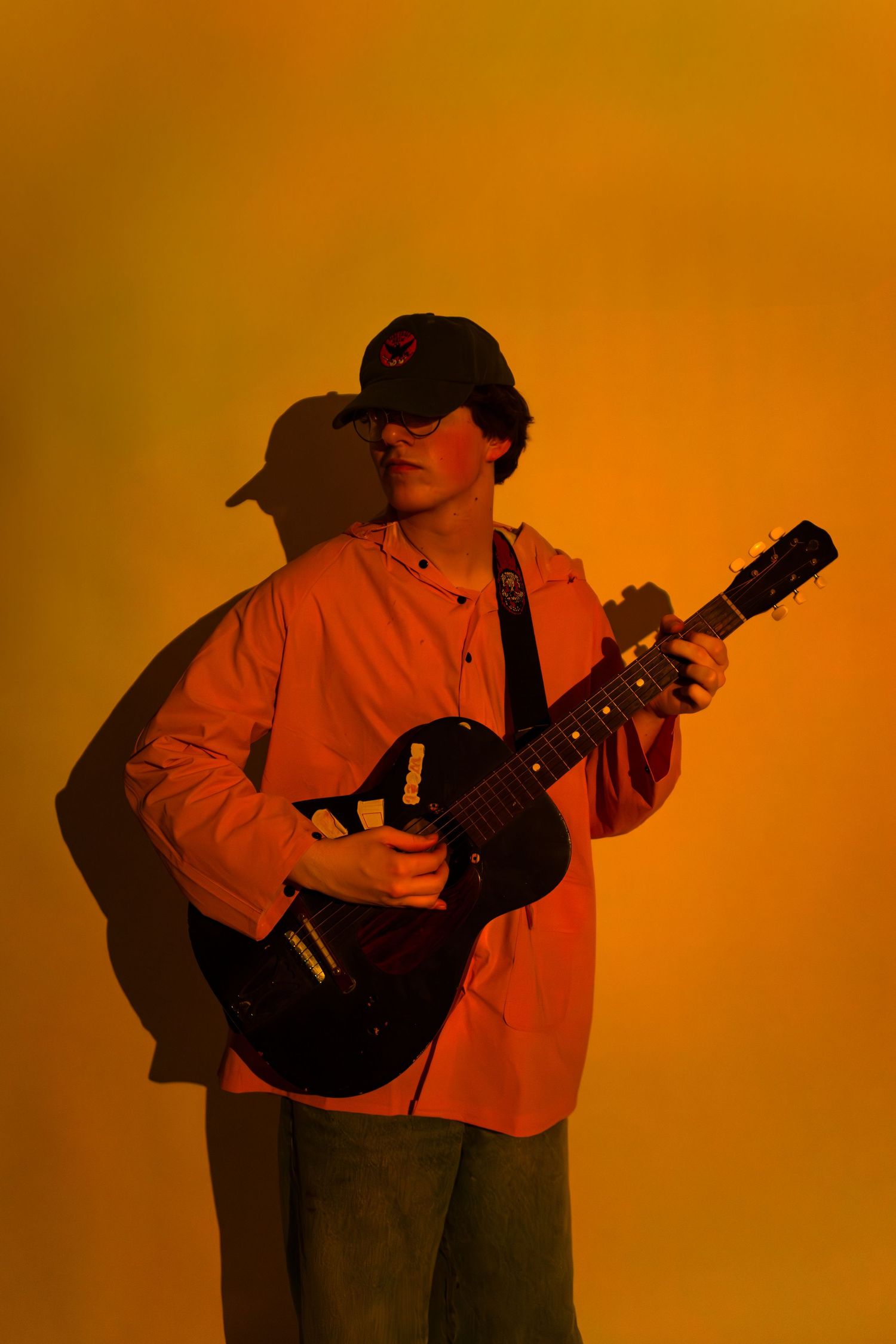 Musician in a red shirt plays ukulele against an orange background creating a series of silhouetted poses.