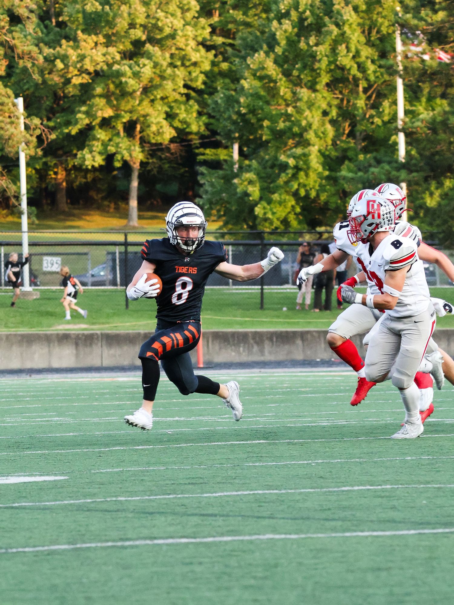 Football player in black uniform running with ball while being chased by defenders in white.