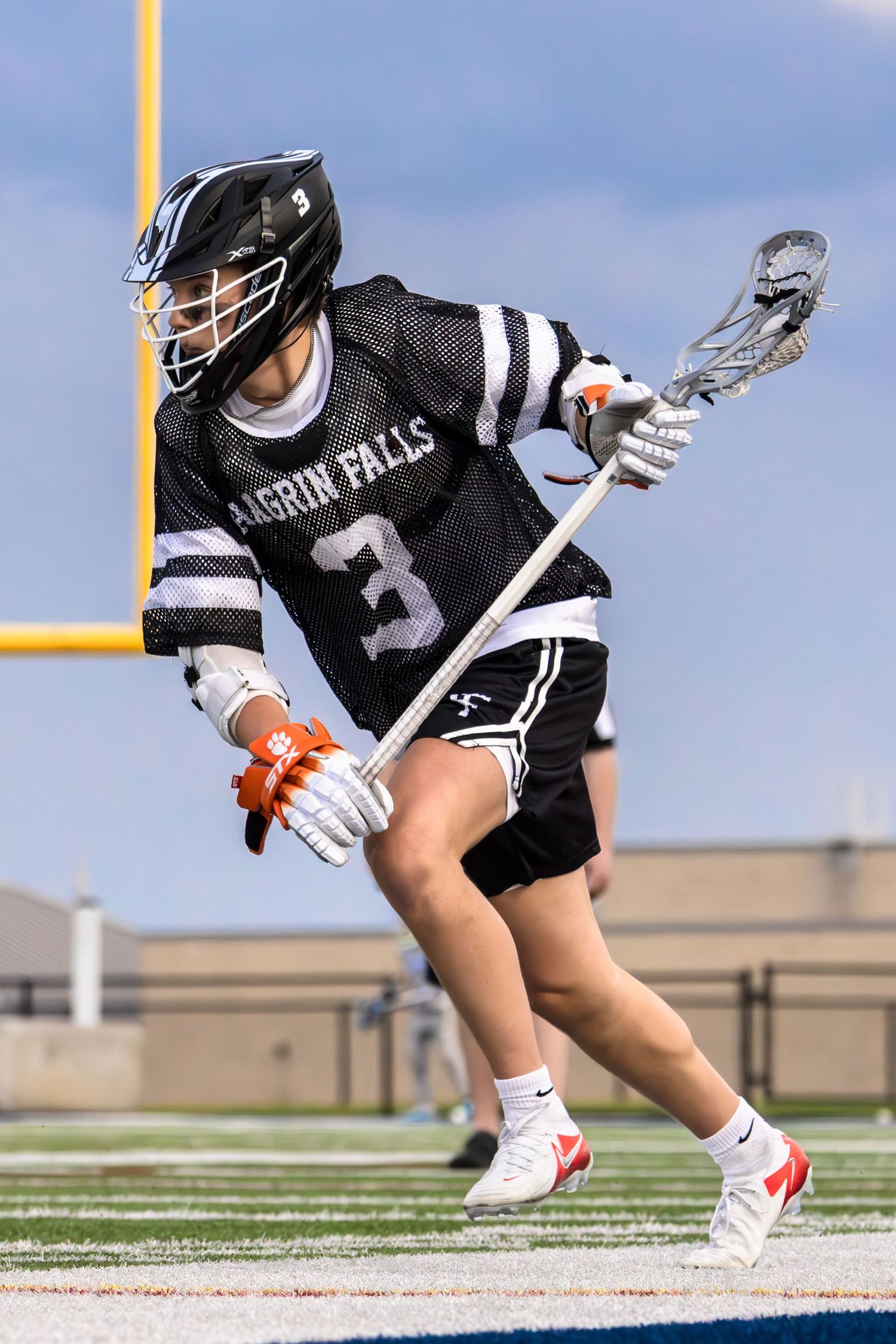 Lacrosse player in black uniform cradles ball while running on field.