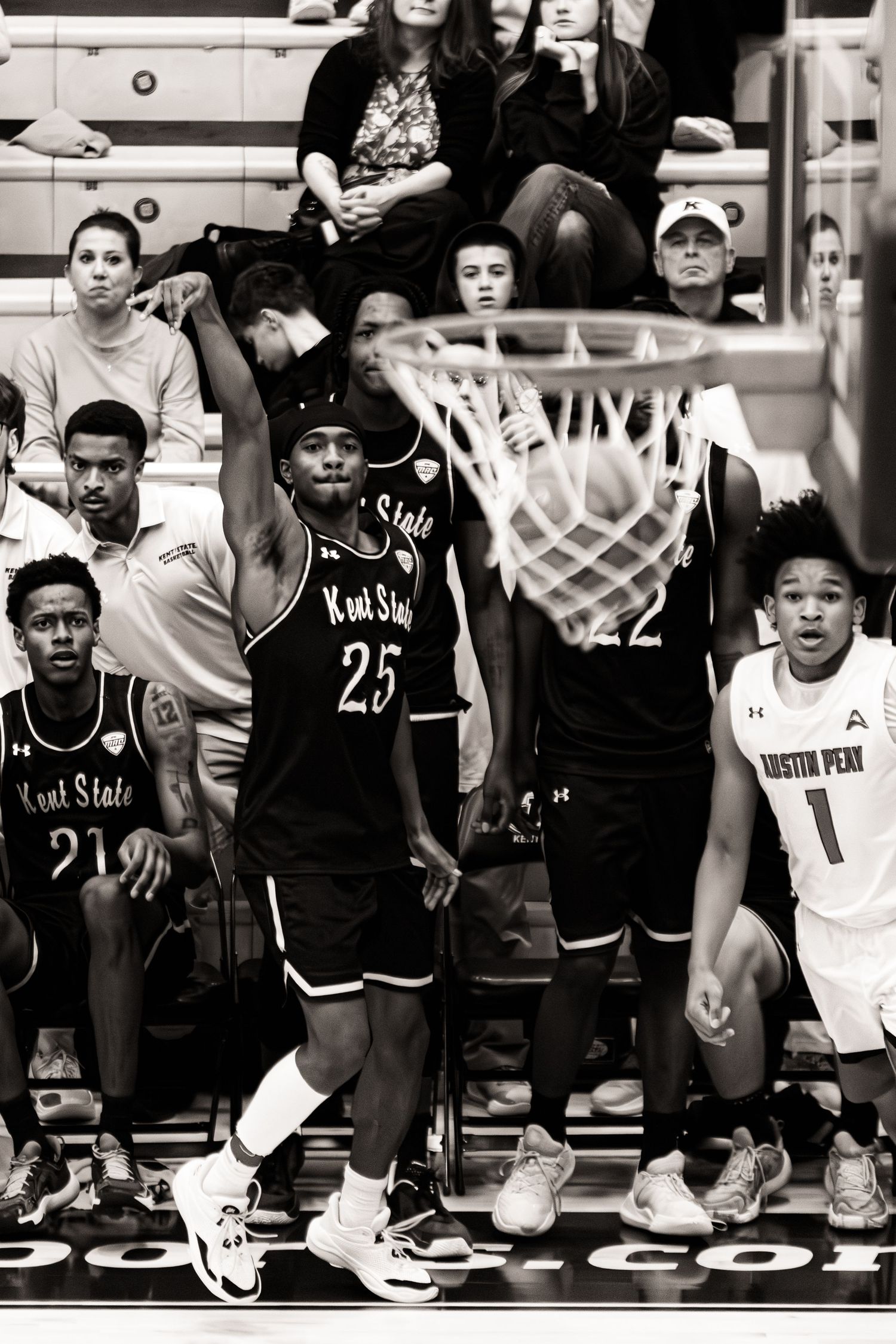 Basketball players sit on the sideline bench during a game wearing black and white uniforms.