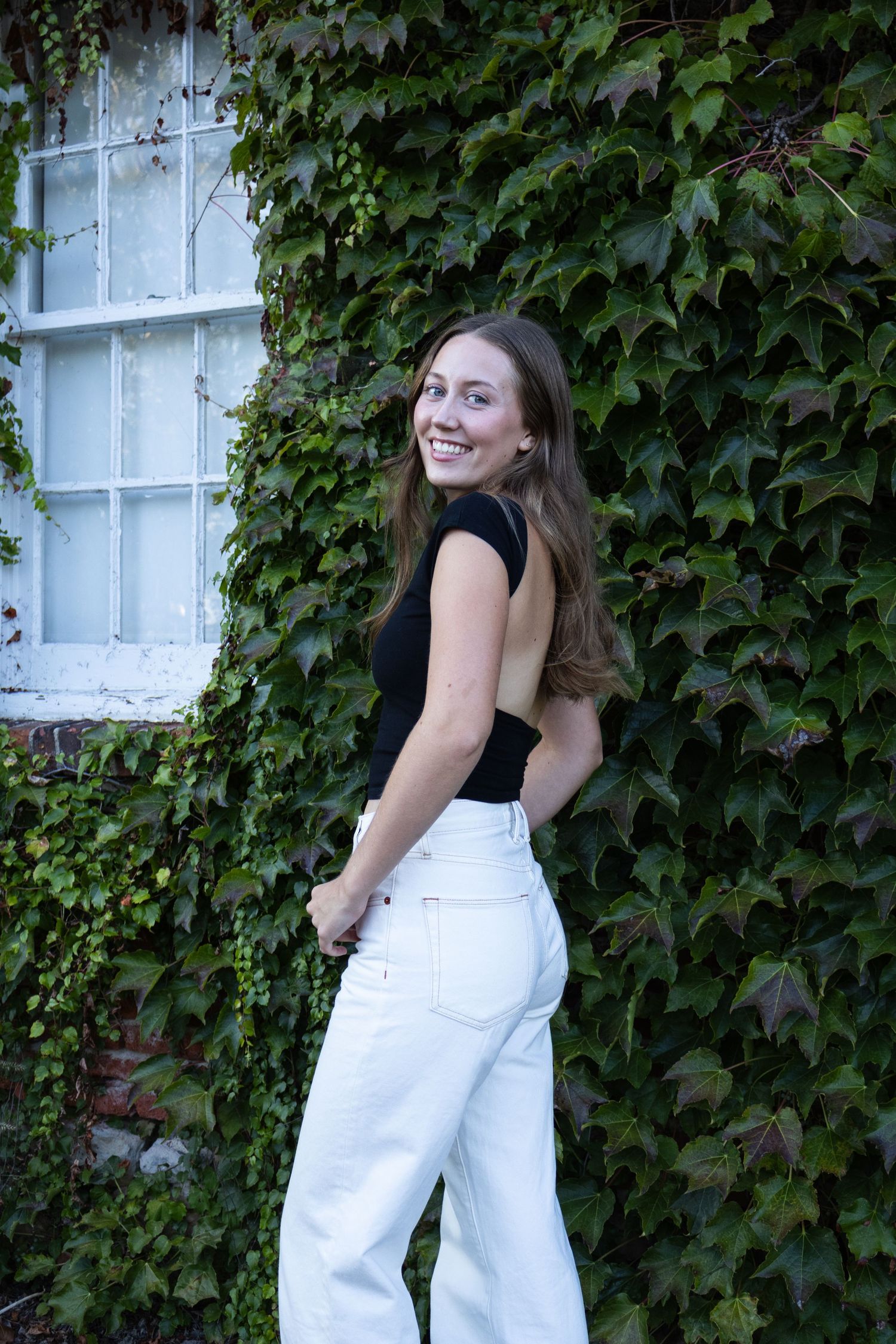 Person wearing white overalls poses playfully against ivy-covered wall in a series of candid shots.
