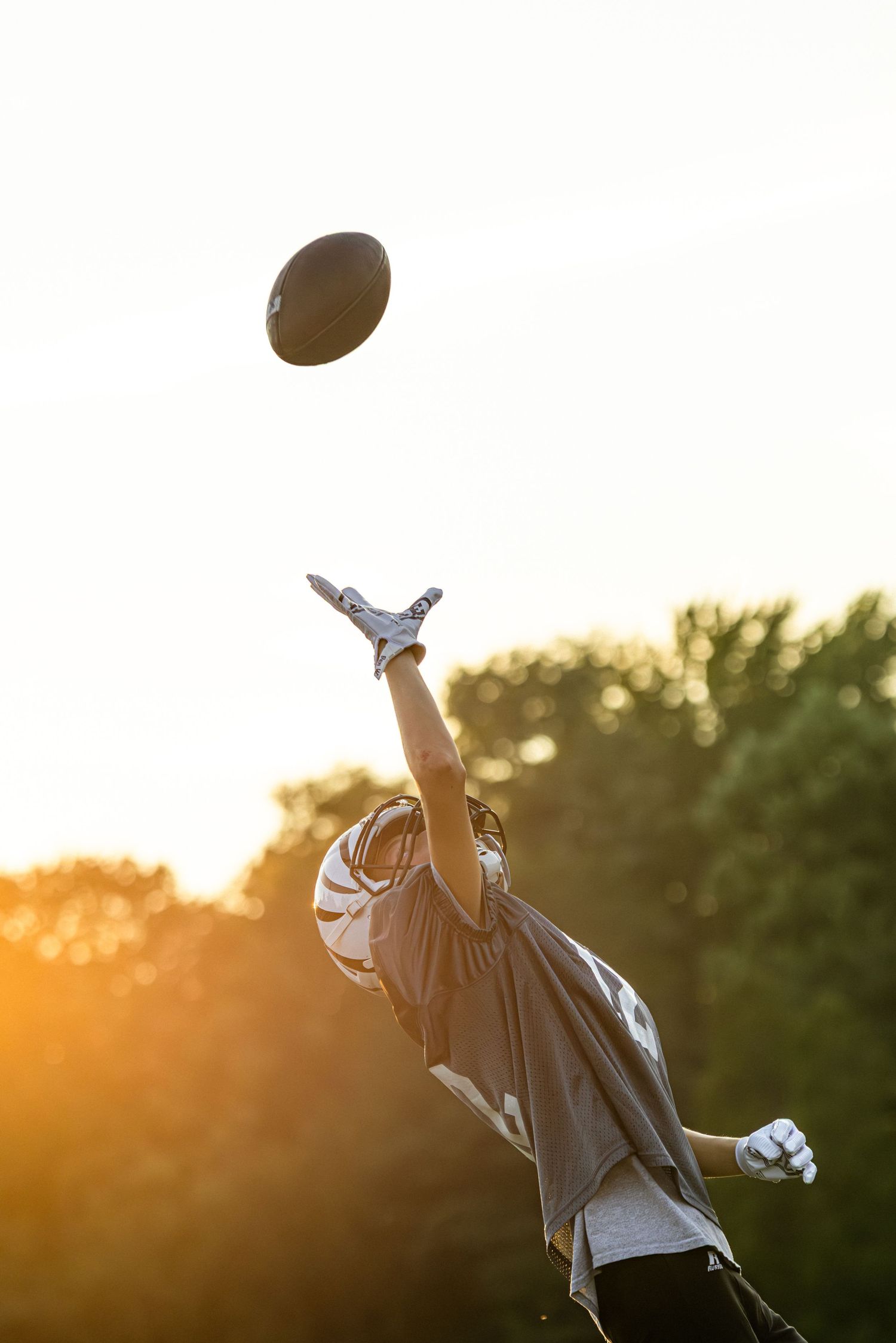 Football flying through the air against a golden sunset sky during practice.