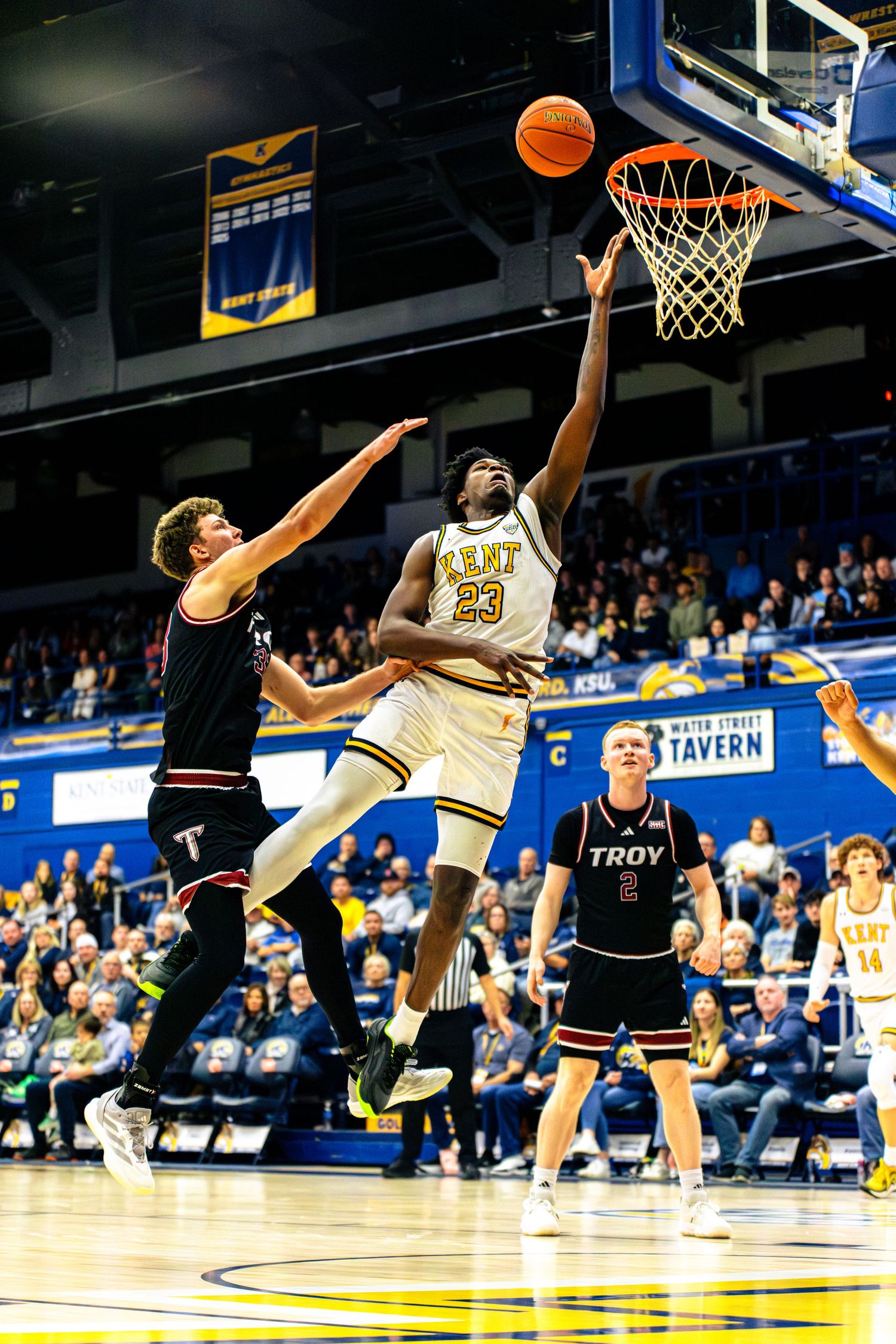 College basketball players leap for the ball during an intense game between Troy and an opposing team on the court.
