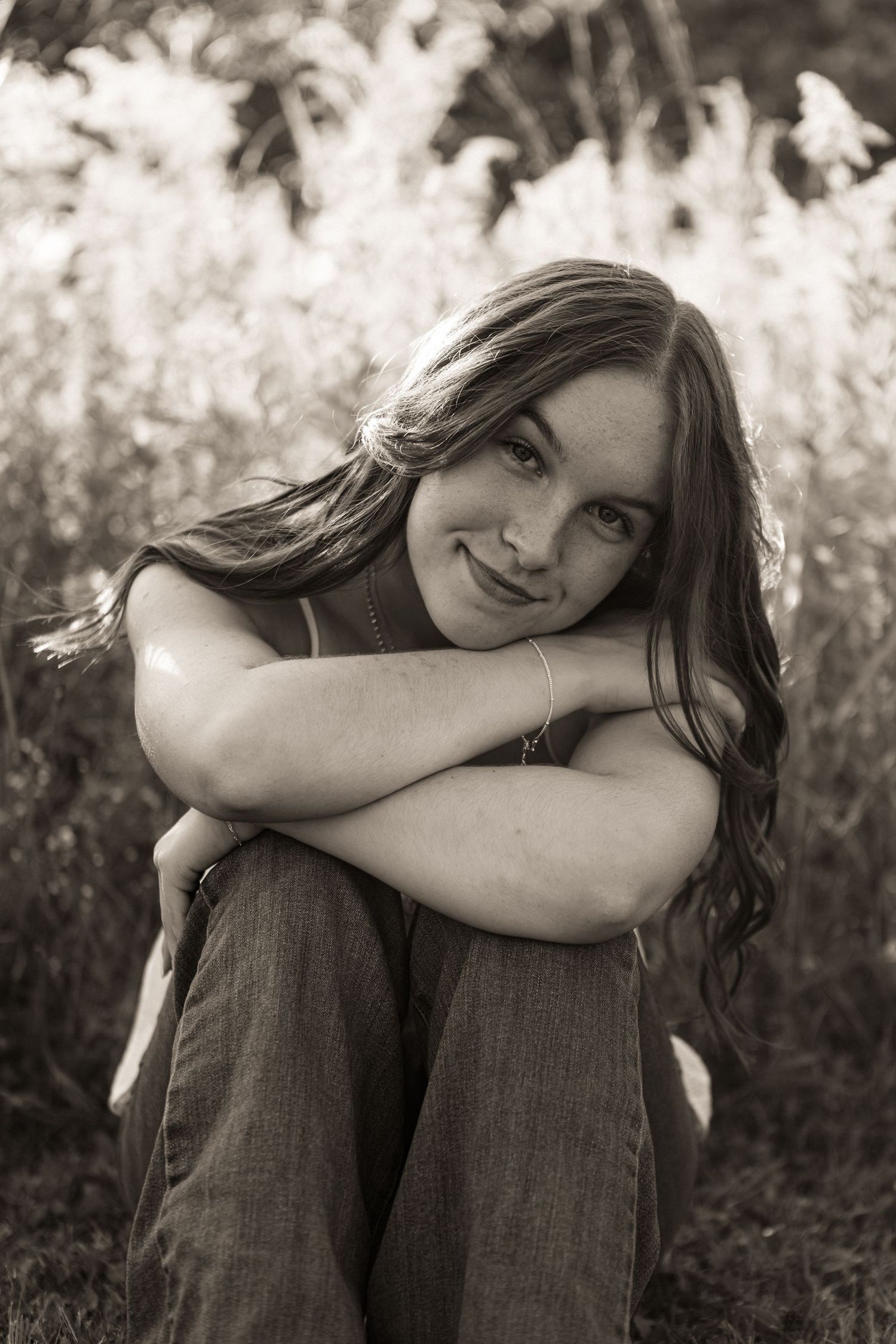Black and white outdoor portrait series showing a person sitting with knees drawn up in a relaxed, casual pose.