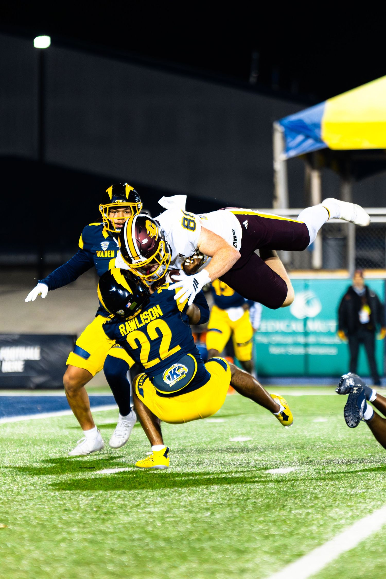 Football player in yellow and black uniform dives horizontally to make a dramatic catch during a game.