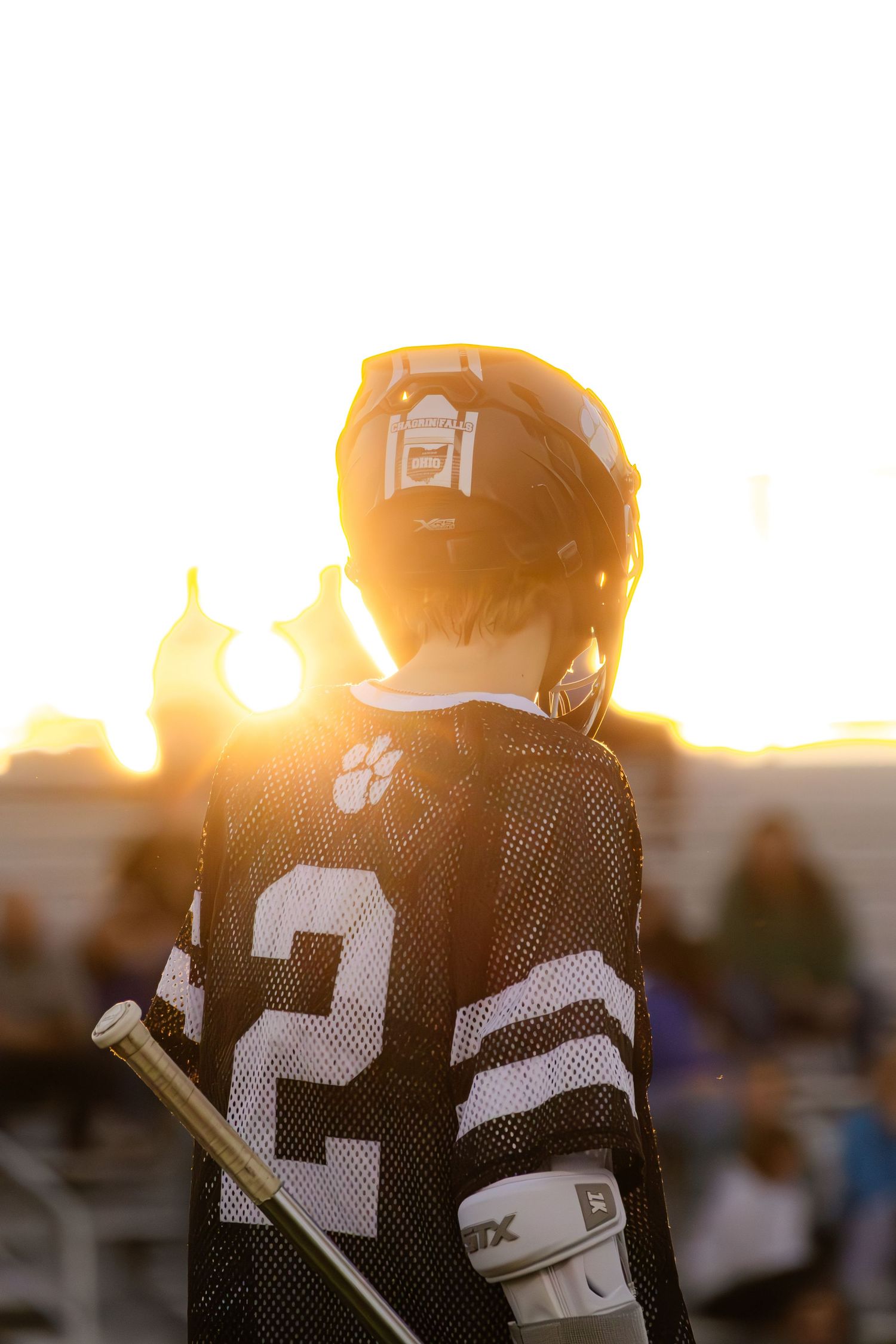Silhouette of lacrosse player in jersey against golden sunset background.