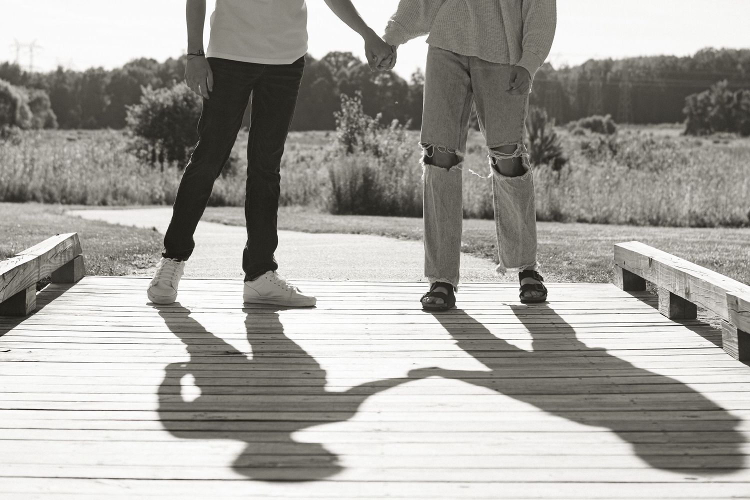 Two pairs of feet cast long shadows on a wooden boardwalk in summer sunlight.