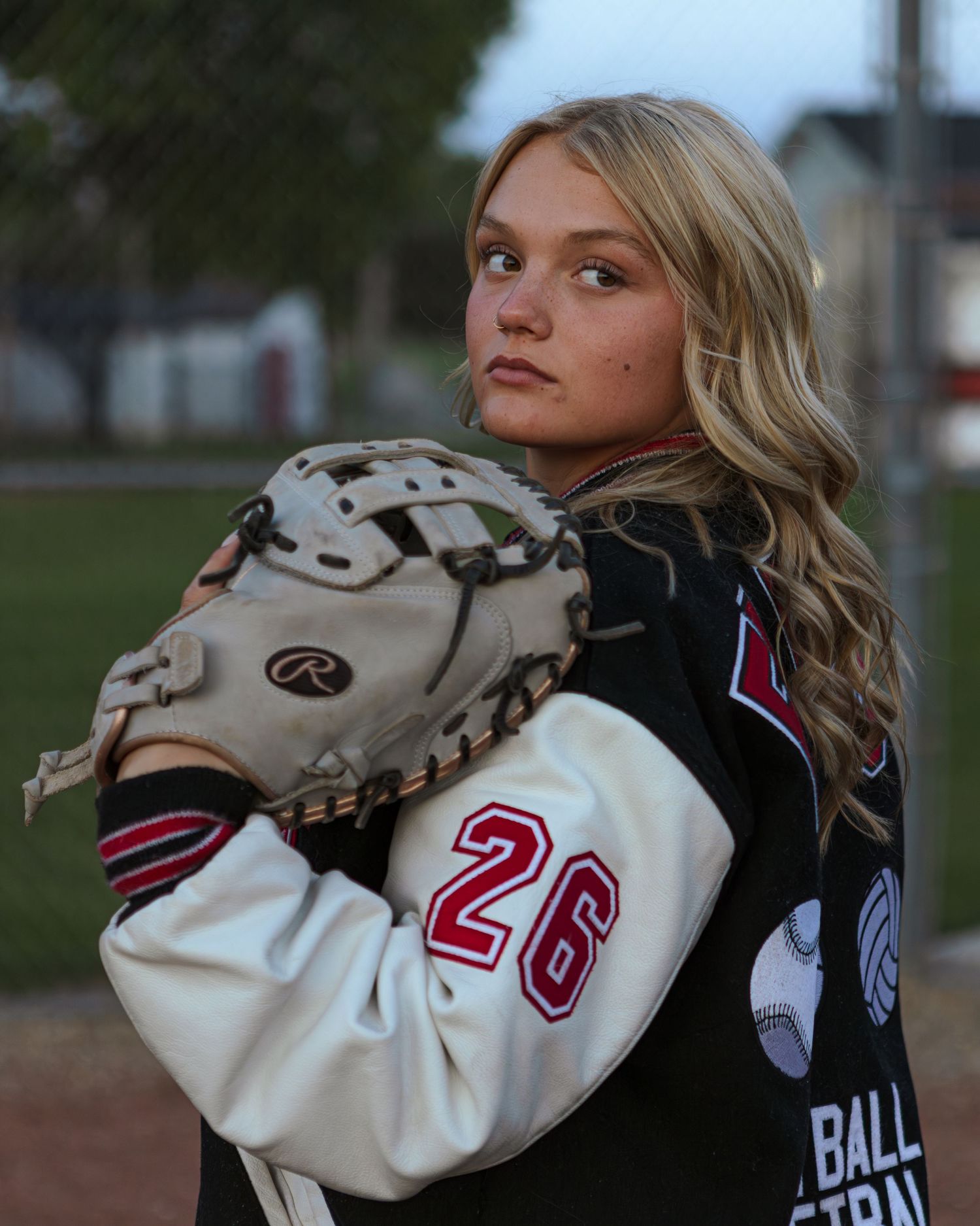 A softball player in a dark uniform with number 20 poses with a glove at dusk.