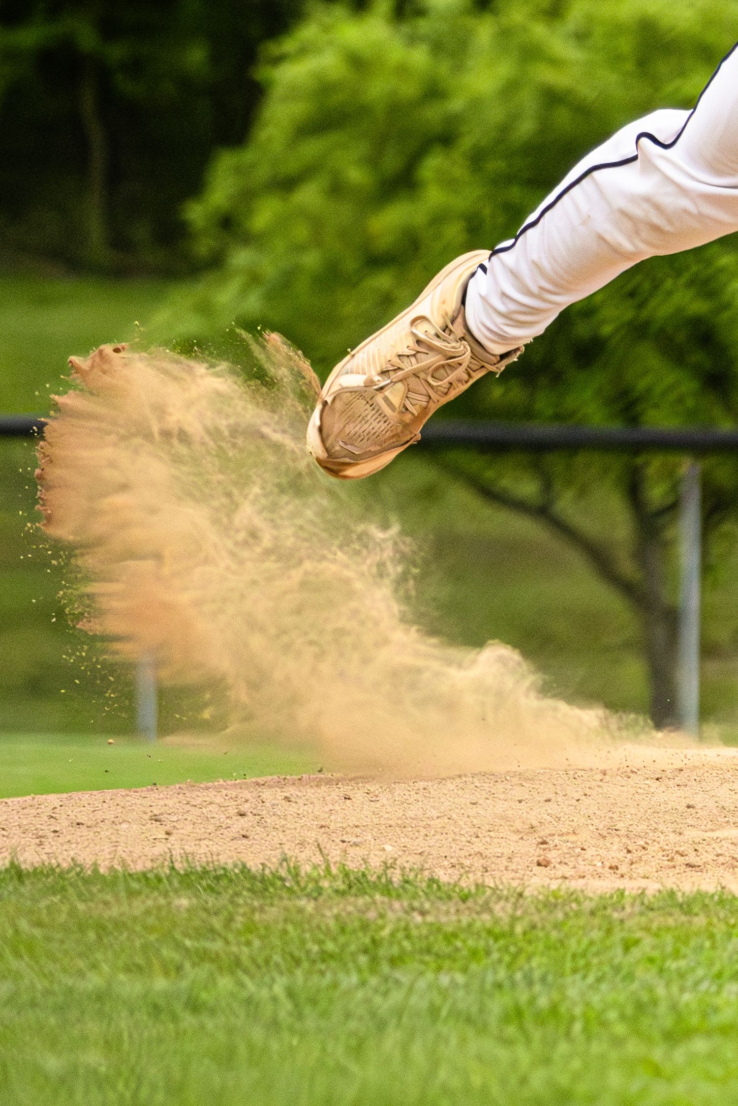 Baseball player's cleat kicking up dirt cloud on baseball diamond during game.