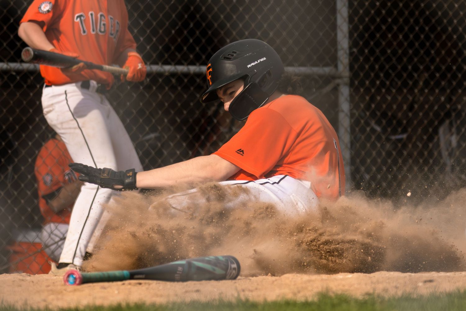 Baseball player slides into base creating cloud of dust during game.