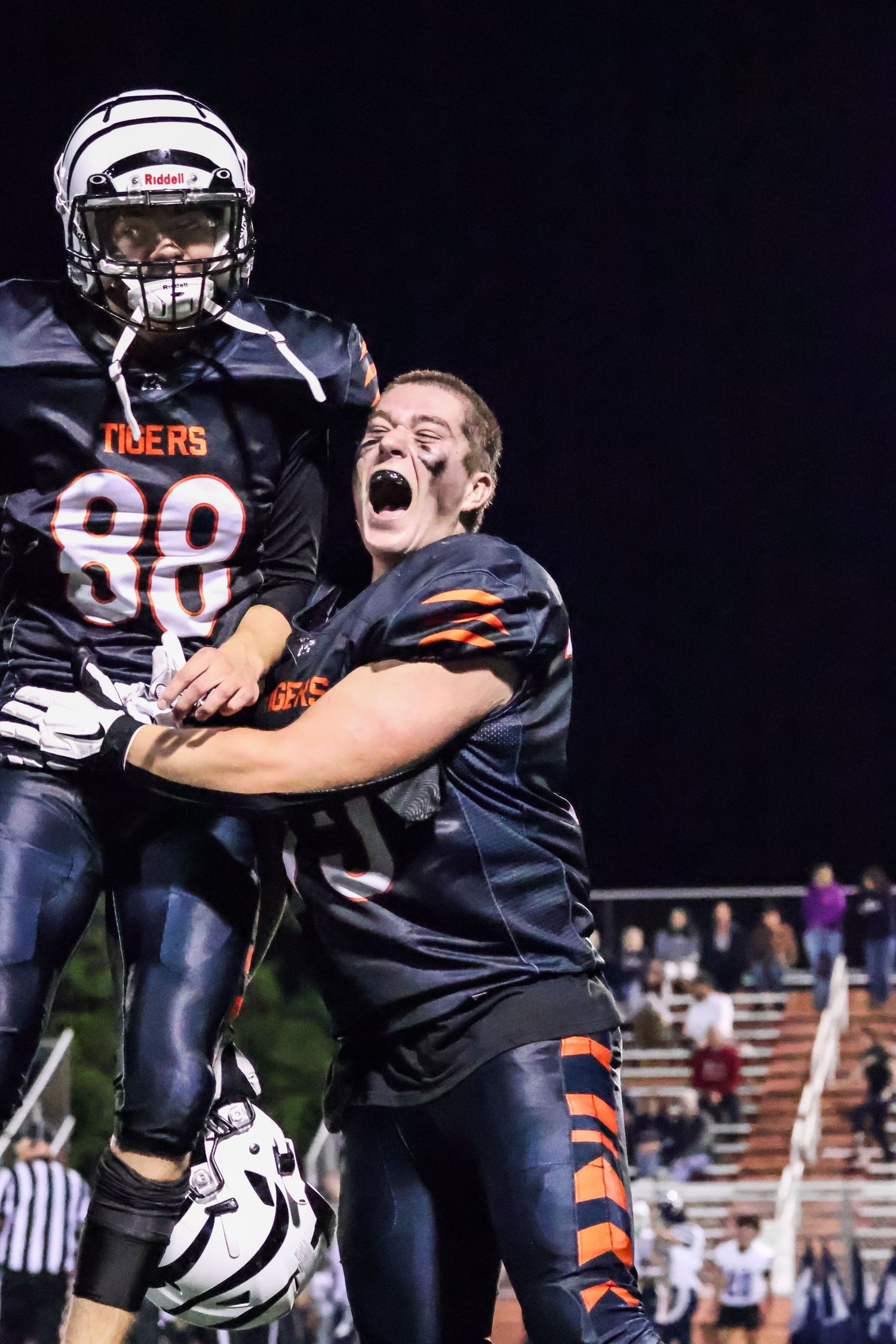 Football teammates celebrating and embracing after scoring a touchdown during a night game.