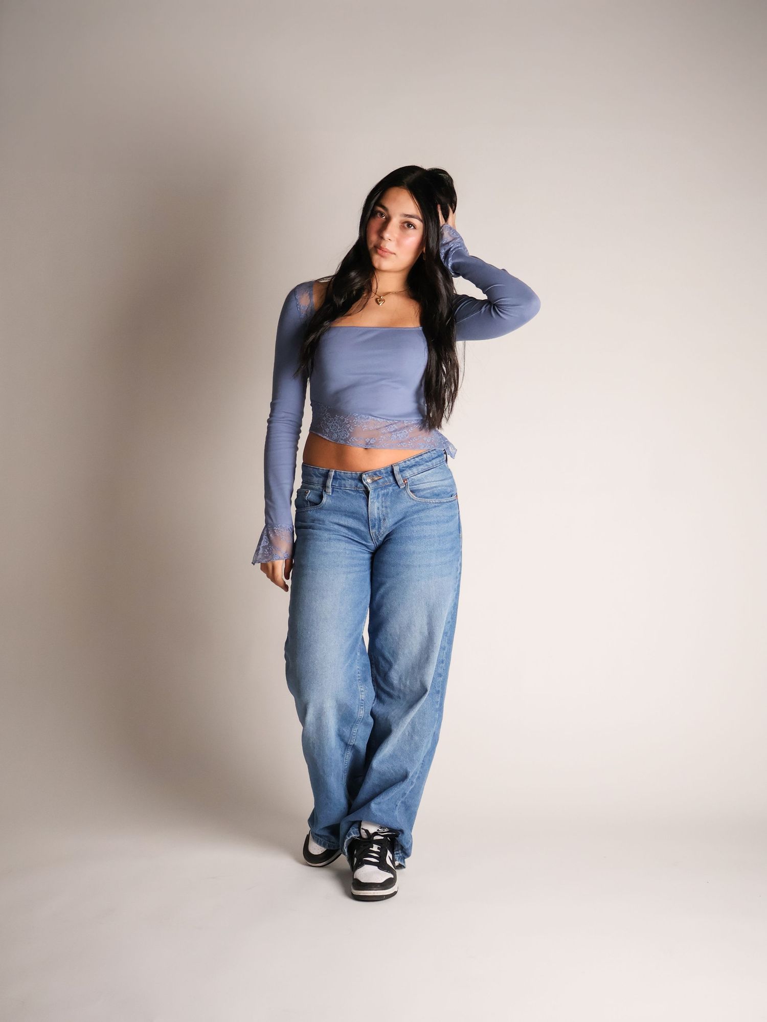 Model in light blue crop top and baggy jeans poses against neutral backdrop in multiple casual poses.