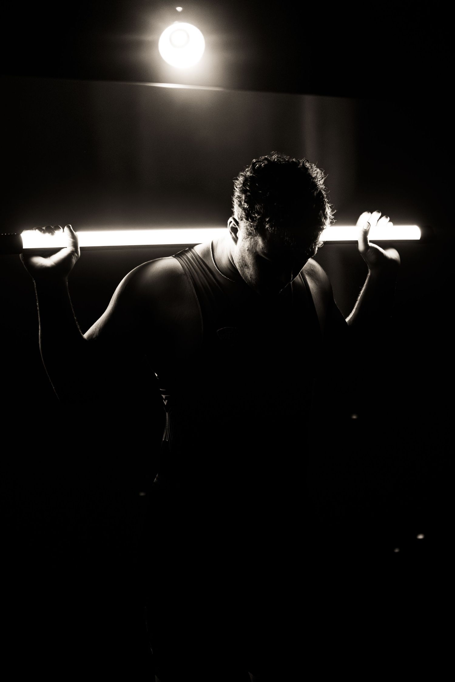 Dramatic silhouette sequence of a person lifting weights against bright backlighting in a dark gym setting.