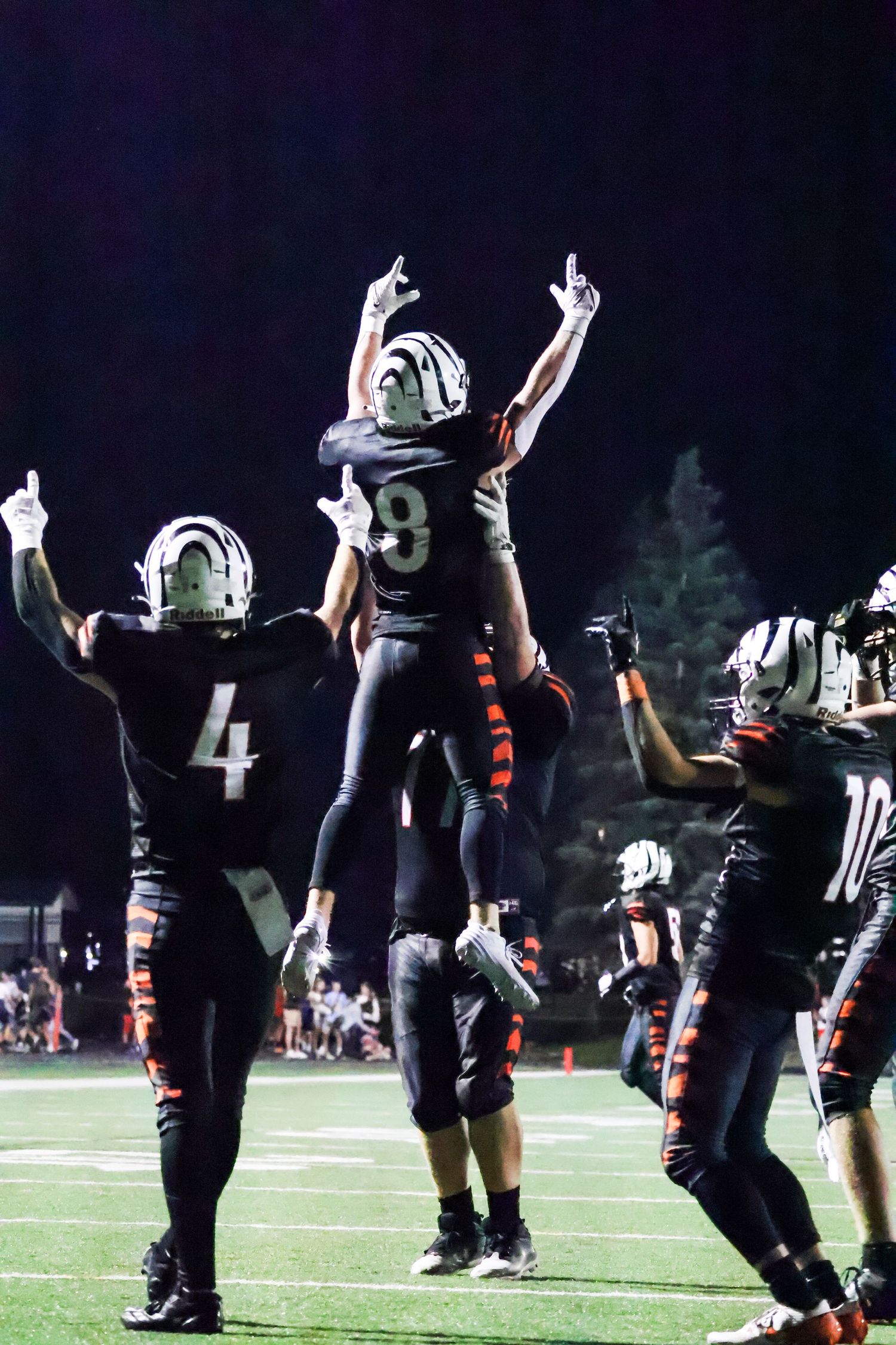 Football players in black uniforms celebrating with raised arms under stadium lights.