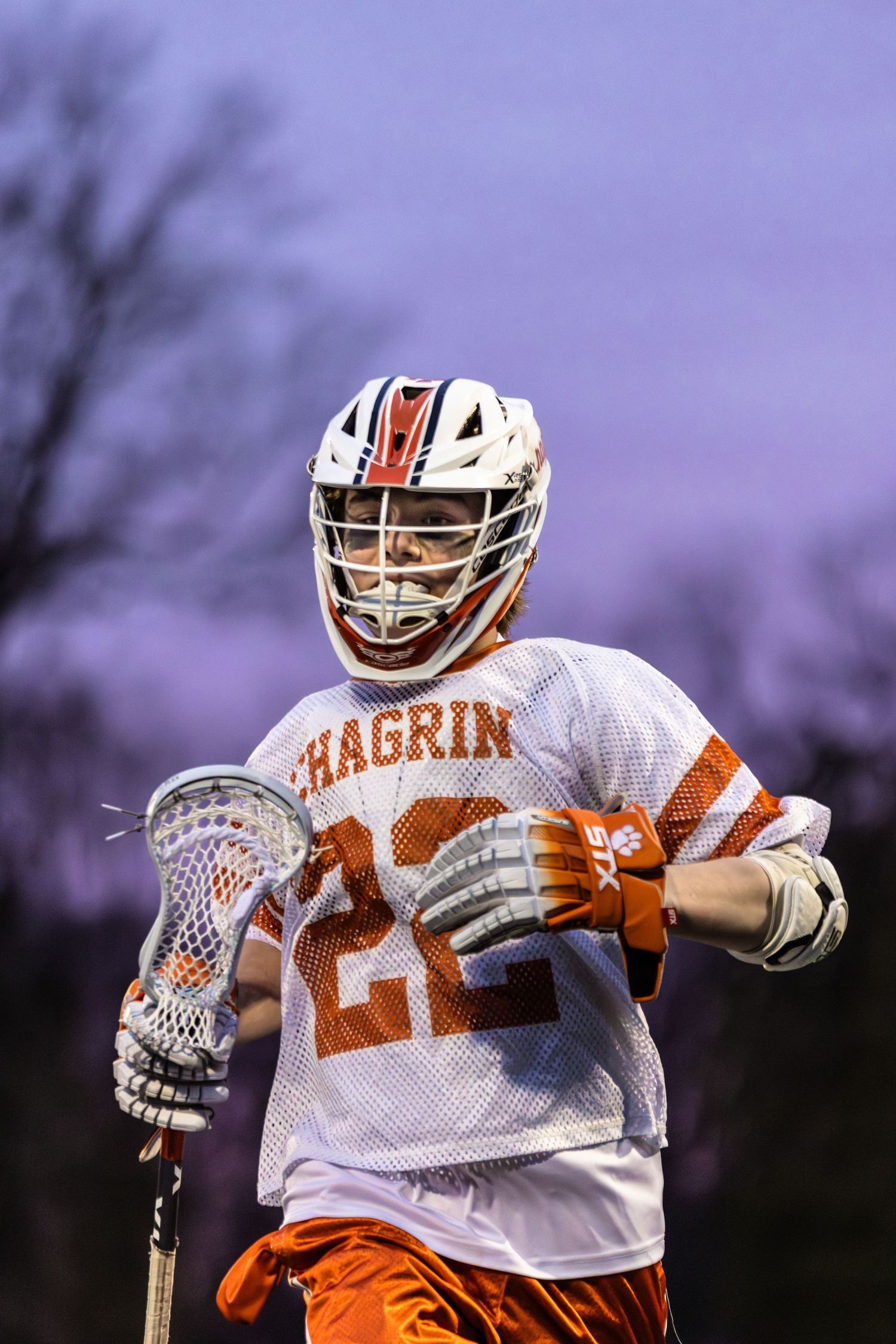 Lacrosse player in Chagrin white and orange uniform holding stick during game.